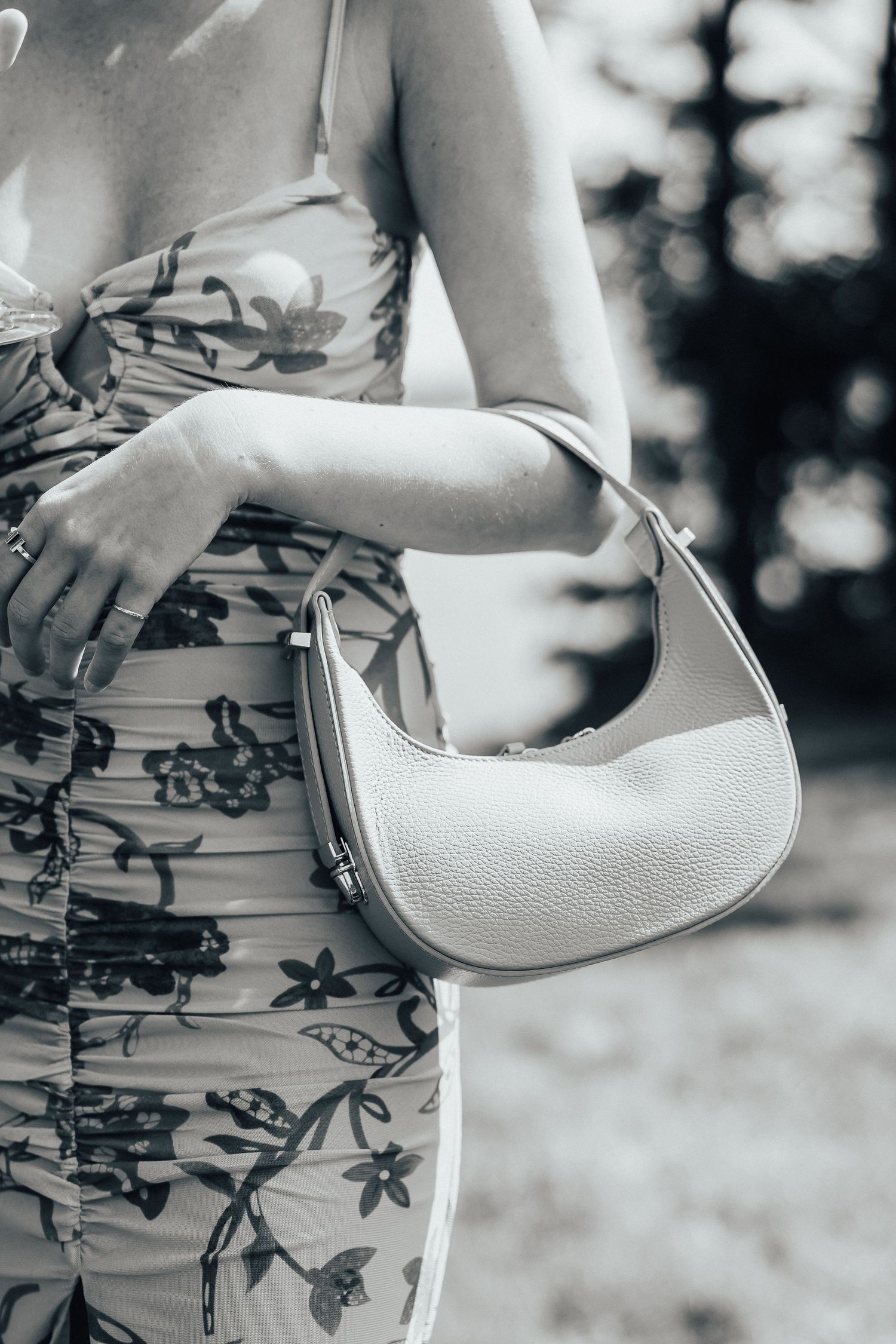 Close-up of a white leather baguette handbag paired with a floral patterned dress in black and white tones.