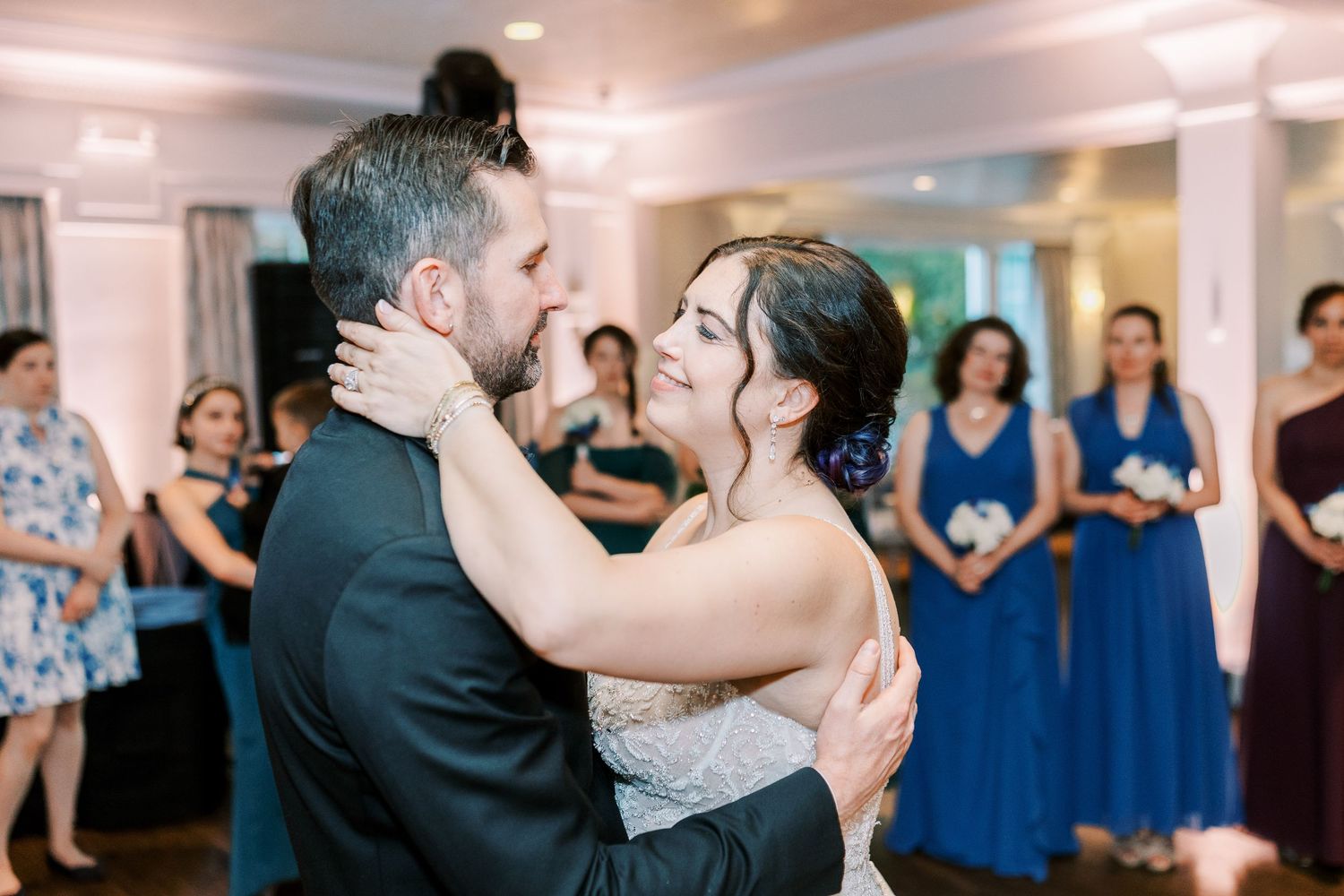 Three couples dancing together at a wedding reception with people watching in formal attire and blue dresses in background.