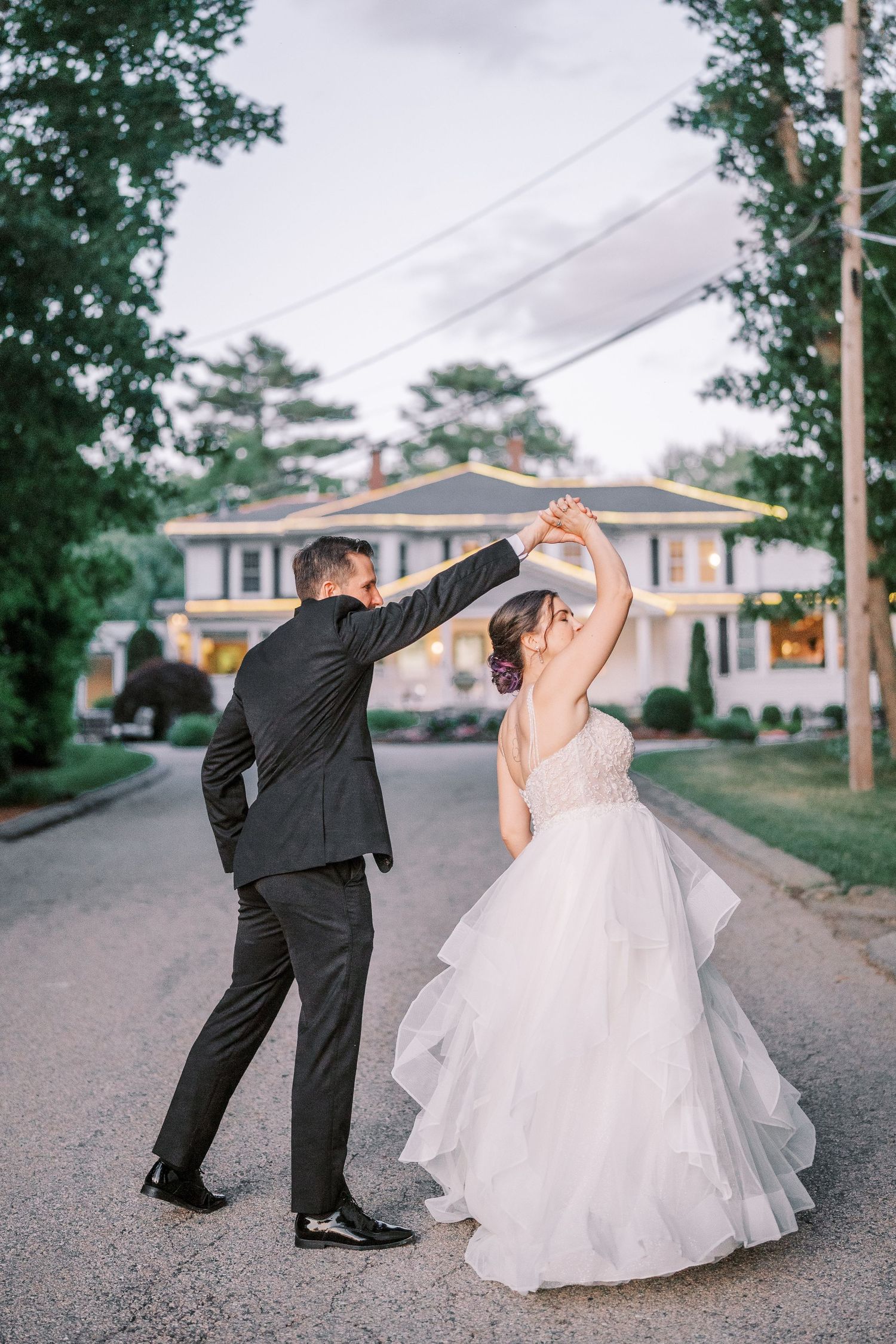 Newlywed couple dancing together on a suburban street with the bride in a flowing white gown and groom in dark suit.