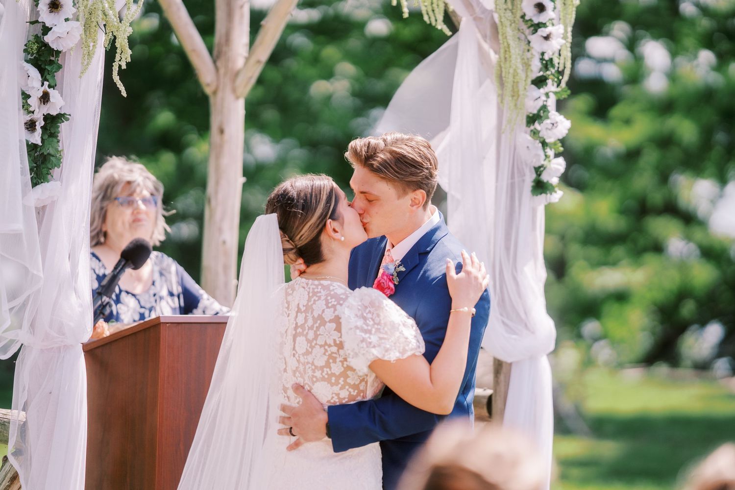 Two wedding ceremony moments showing couples celebrating under white floral-decorated outdoor arches during a summer event.