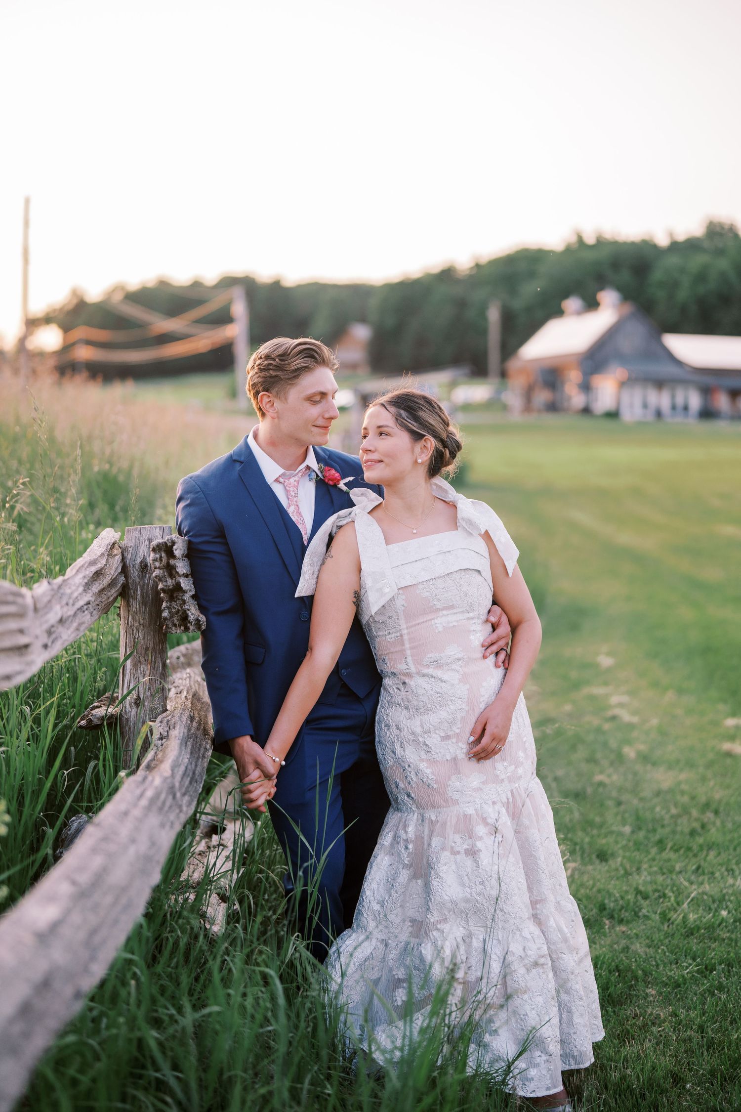 A couple in wedding attire embrace on a grassy field during golden hour as they share an intimate moment together.