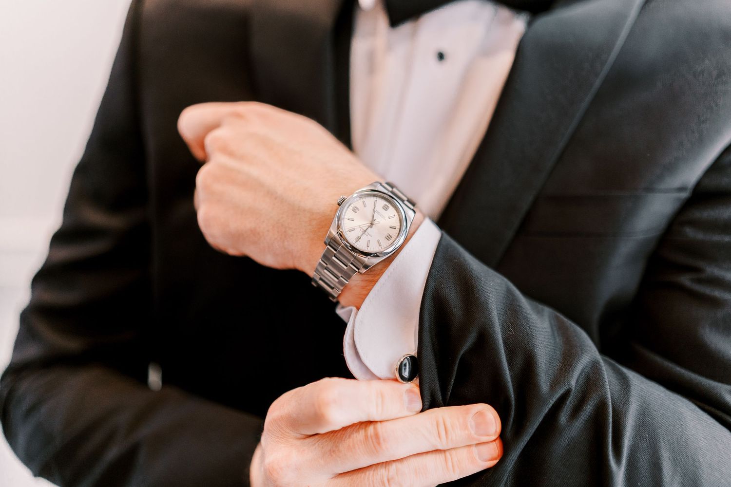 A person wearing a black suit adjusts their cufflinks while displaying an elegant wristwatch.