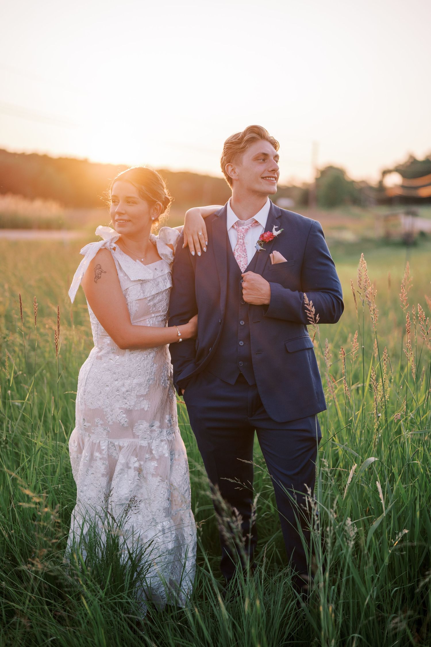 A newlywed couple shares joyful moments in a sunlit field of tall grass at golden hour.