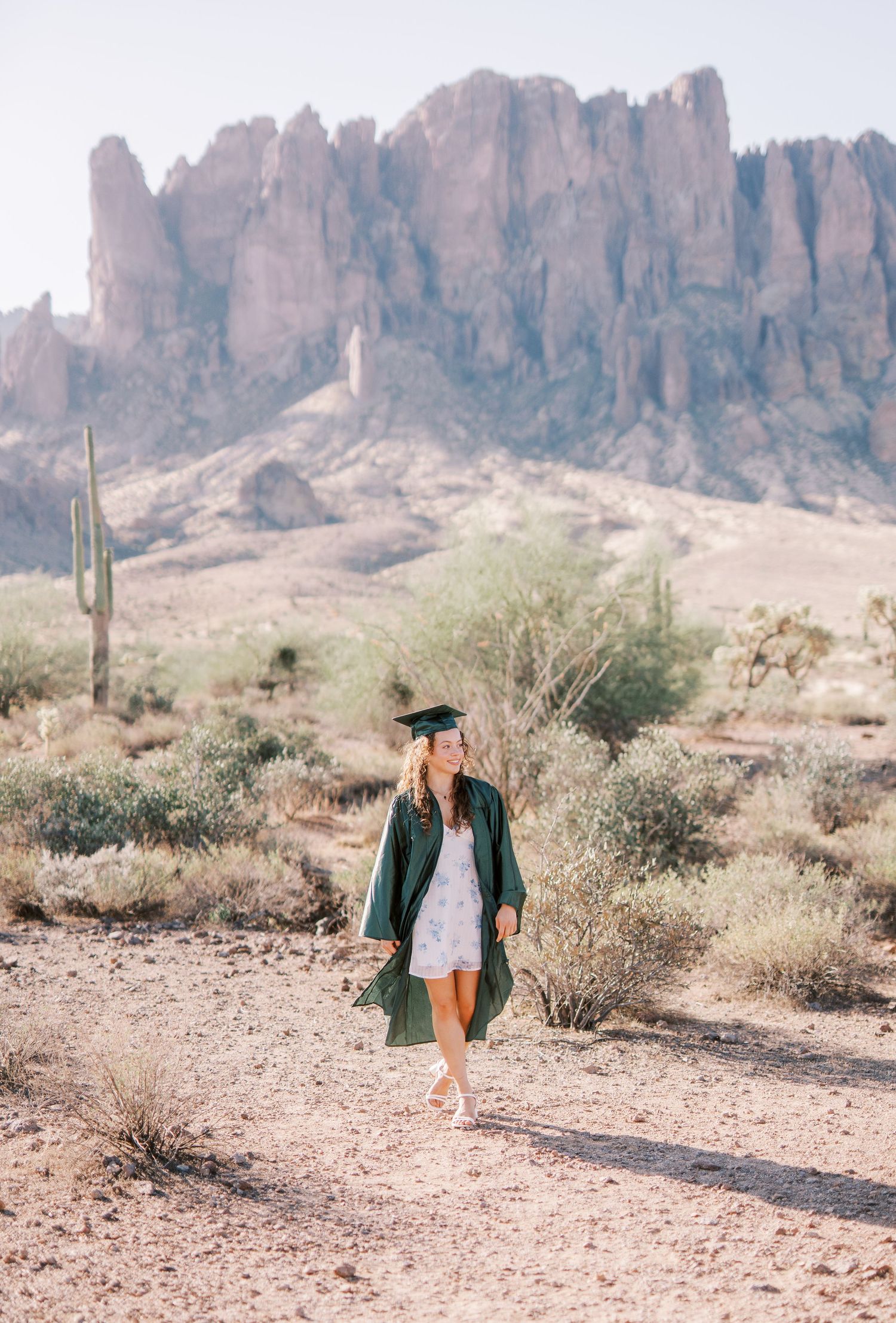 A person walks along a desert trail with rugged mountains and saguaro cacti in the Superstition Mountains of Arizona.