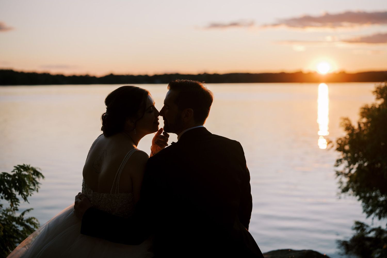 A silhouetted couple sits together by a scenic lake at sunset with golden light reflecting on the water.