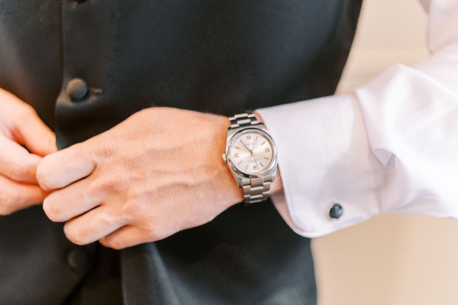 Close-up view of a silver and gold dress watch worn with a formal black suit and white dress shirt.