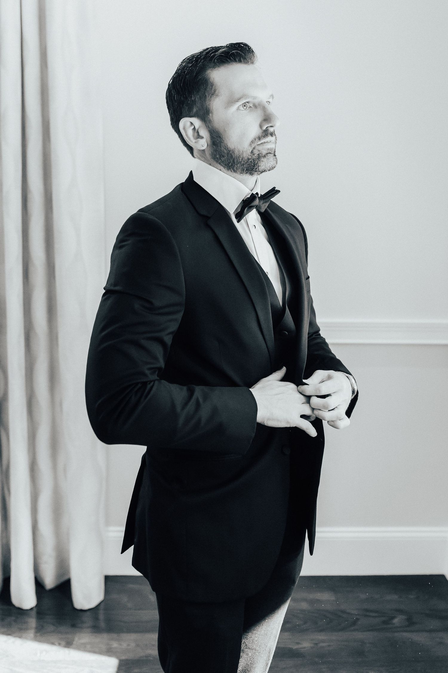 Classic black and white portrait of a person in formal attire adjusting their tuxedo while looking upward.