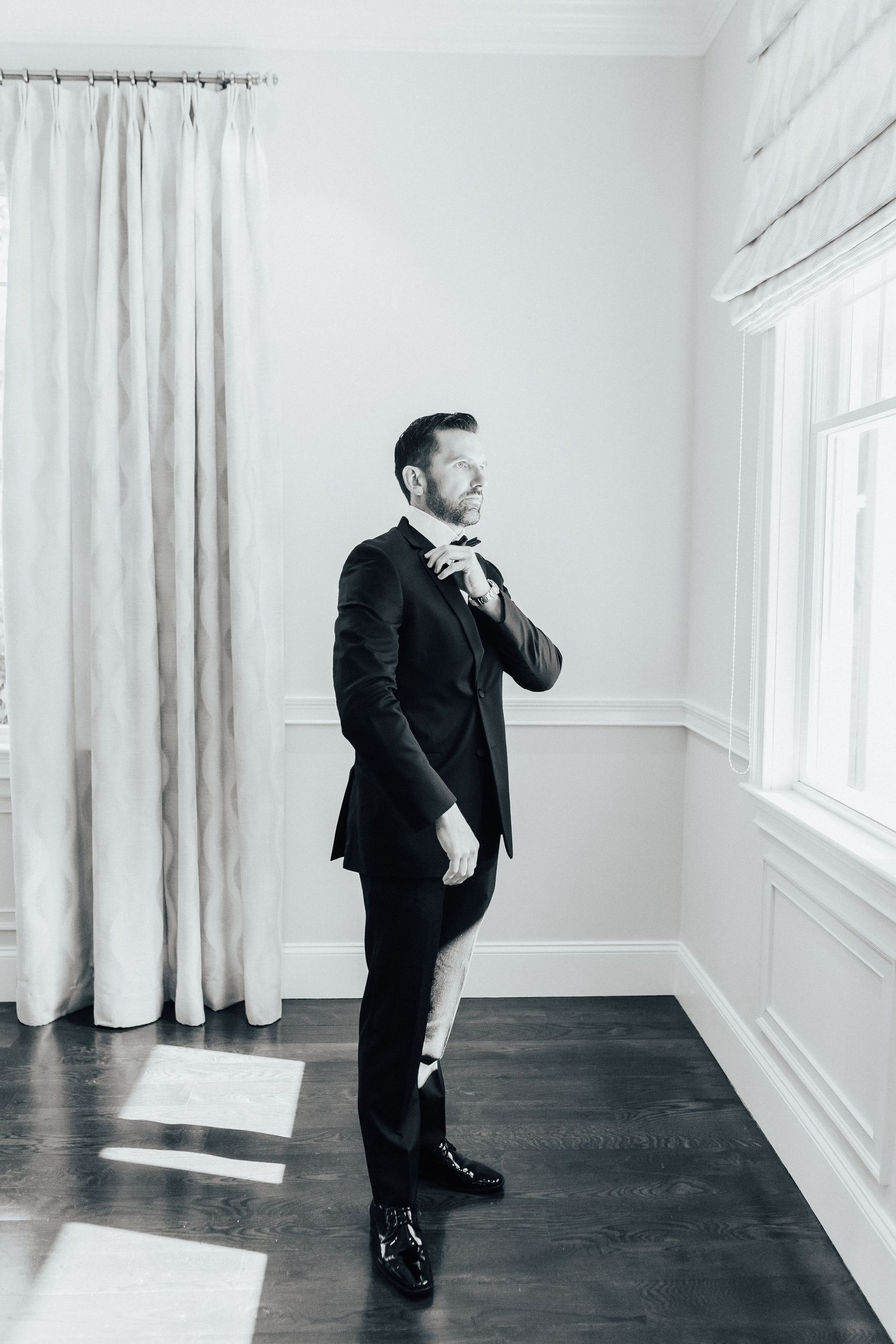 A black and white photo series showing a figure in dark suit standing in different poses in a minimalist white room.