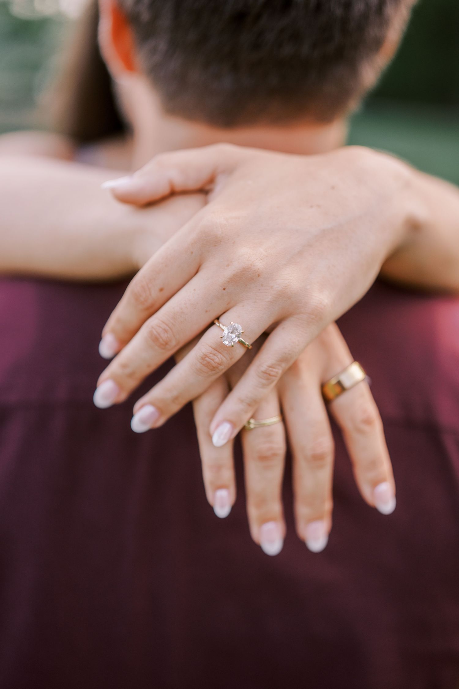 Close up view of hands with engagement rings resting against a burgundy shirt background.