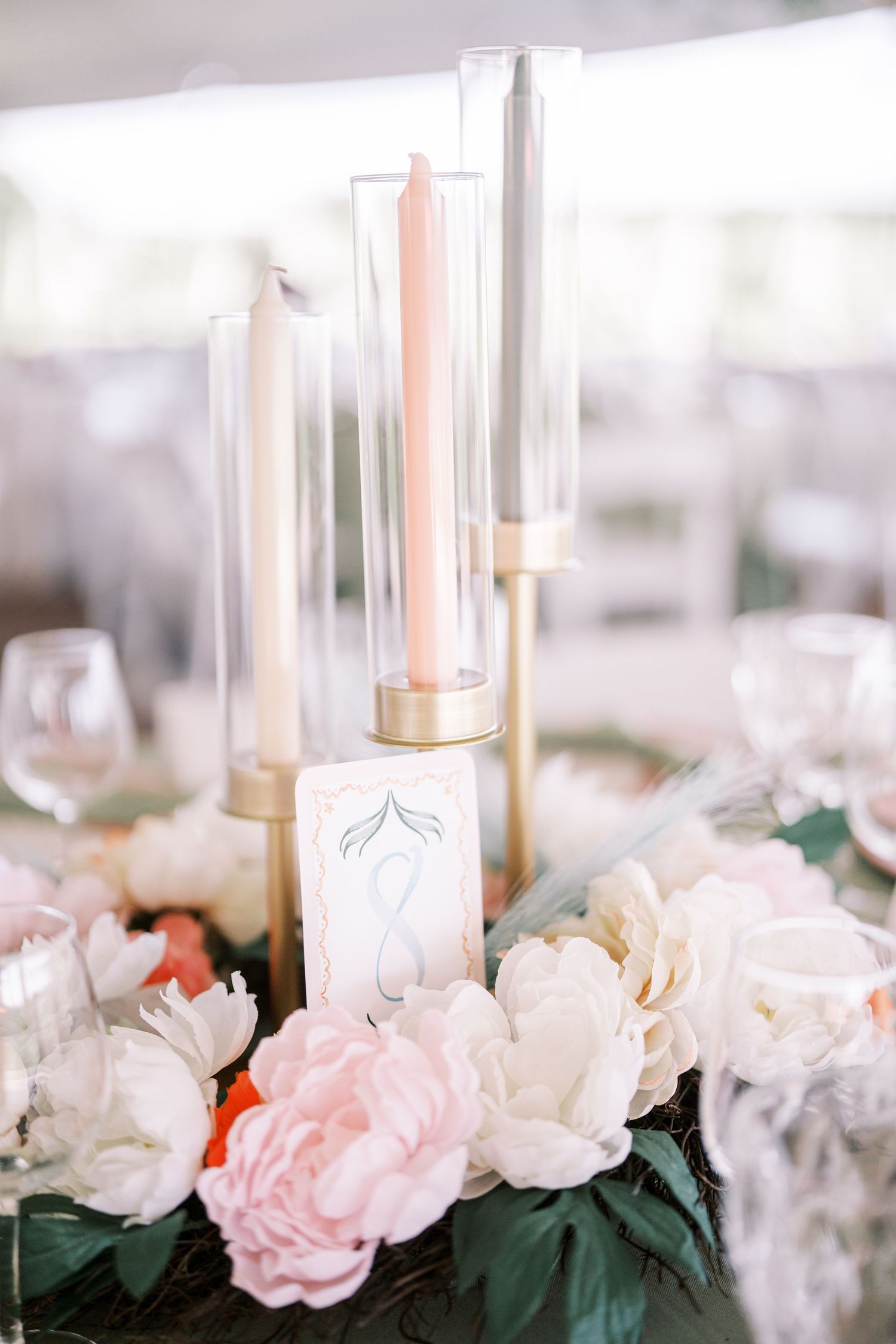 Elegant table centerpiece with pink and white roses surrounding tall taper candles in glass holders for a romantic wedding reception.
