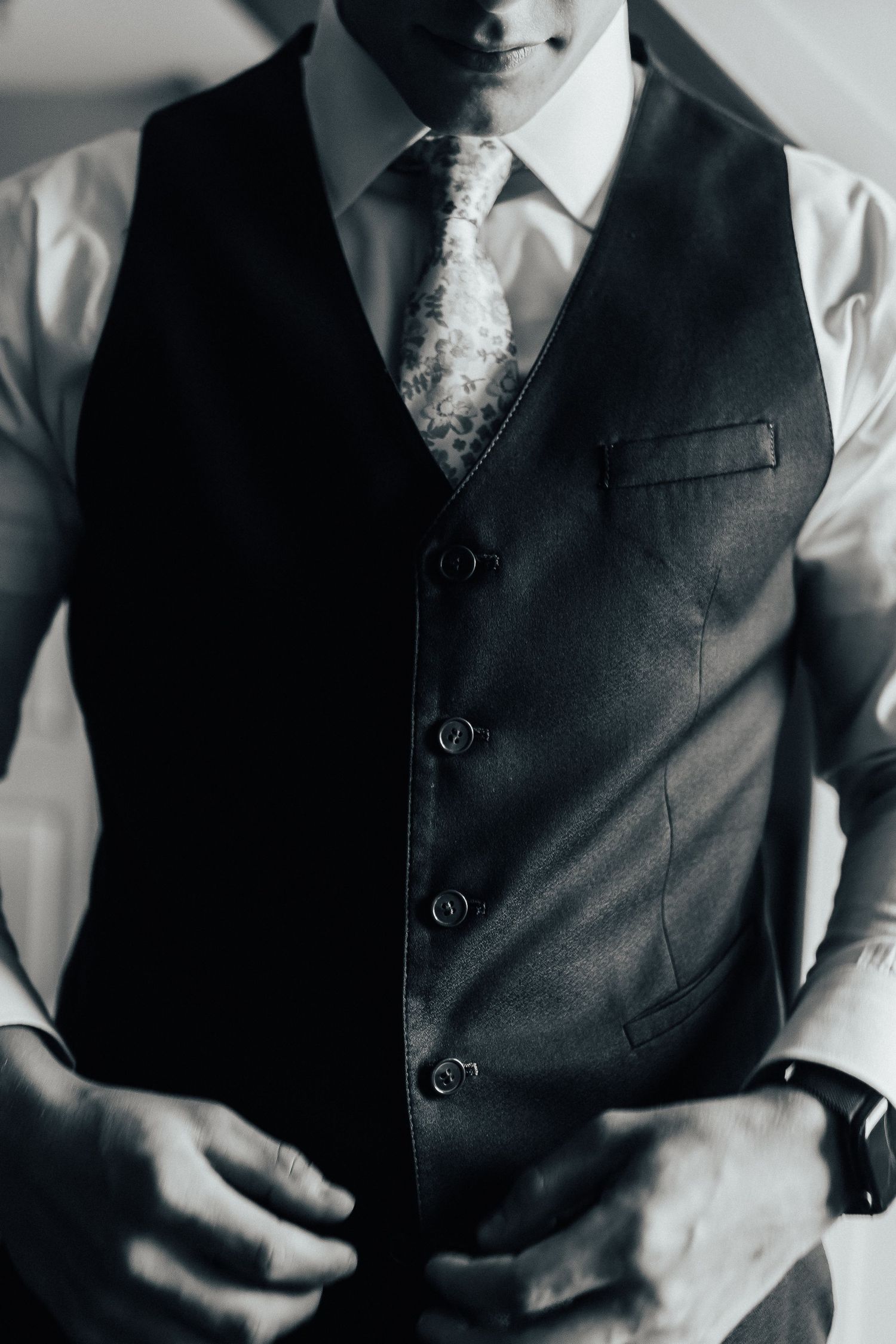 A black and white close-up detail shot of a person wearing a formal dark vest and white dress shirt.