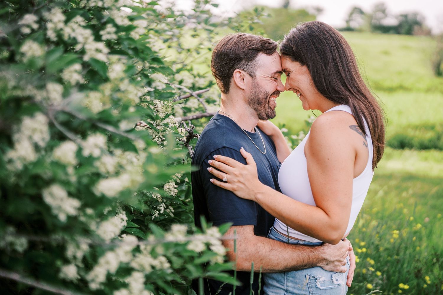 A romantic couple embrace in a sunny meadow surrounded by wildflowers during a spring engagement photoshoot.