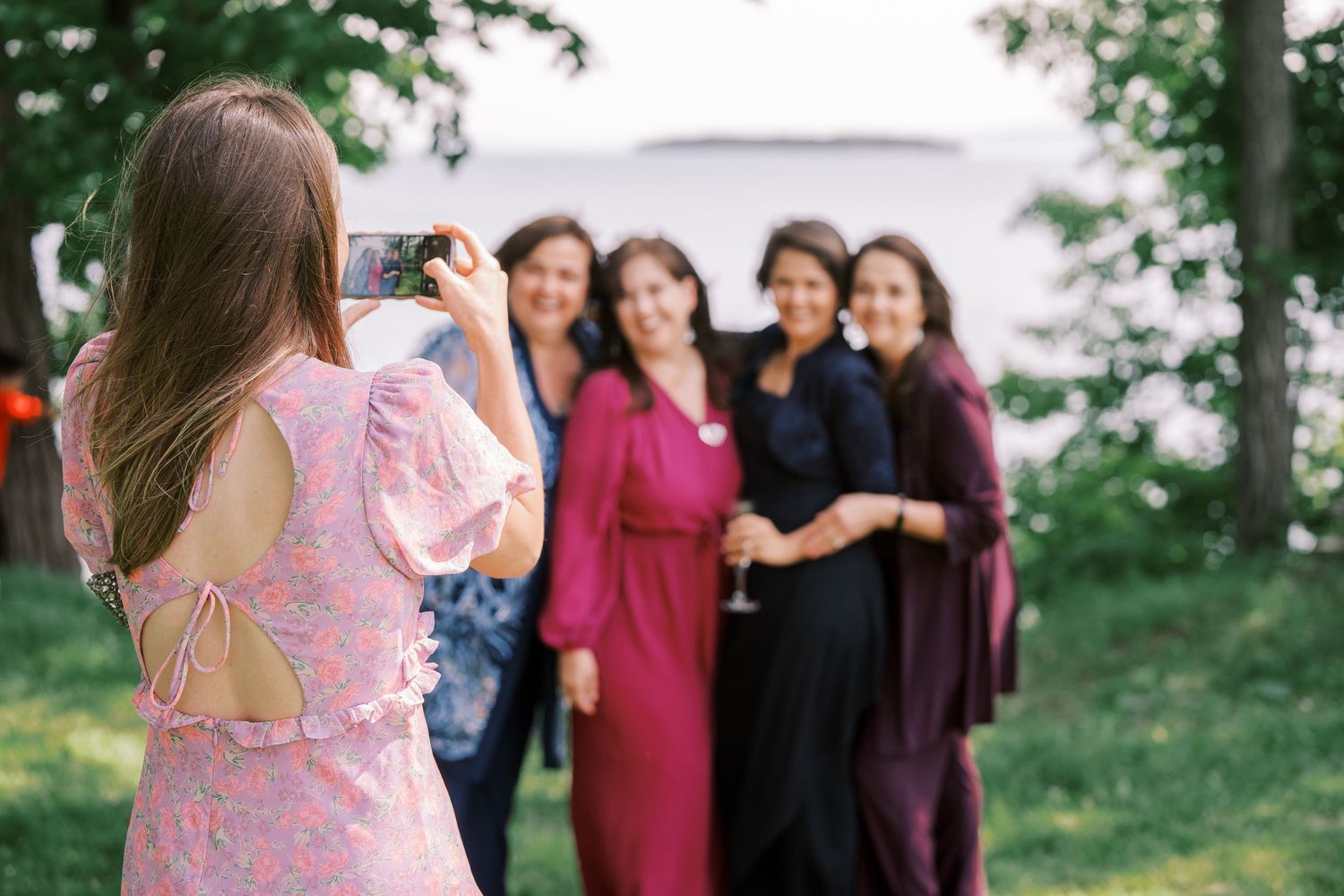 A photographer in pink dress takes a photo of guests posing together outdoors during an event.