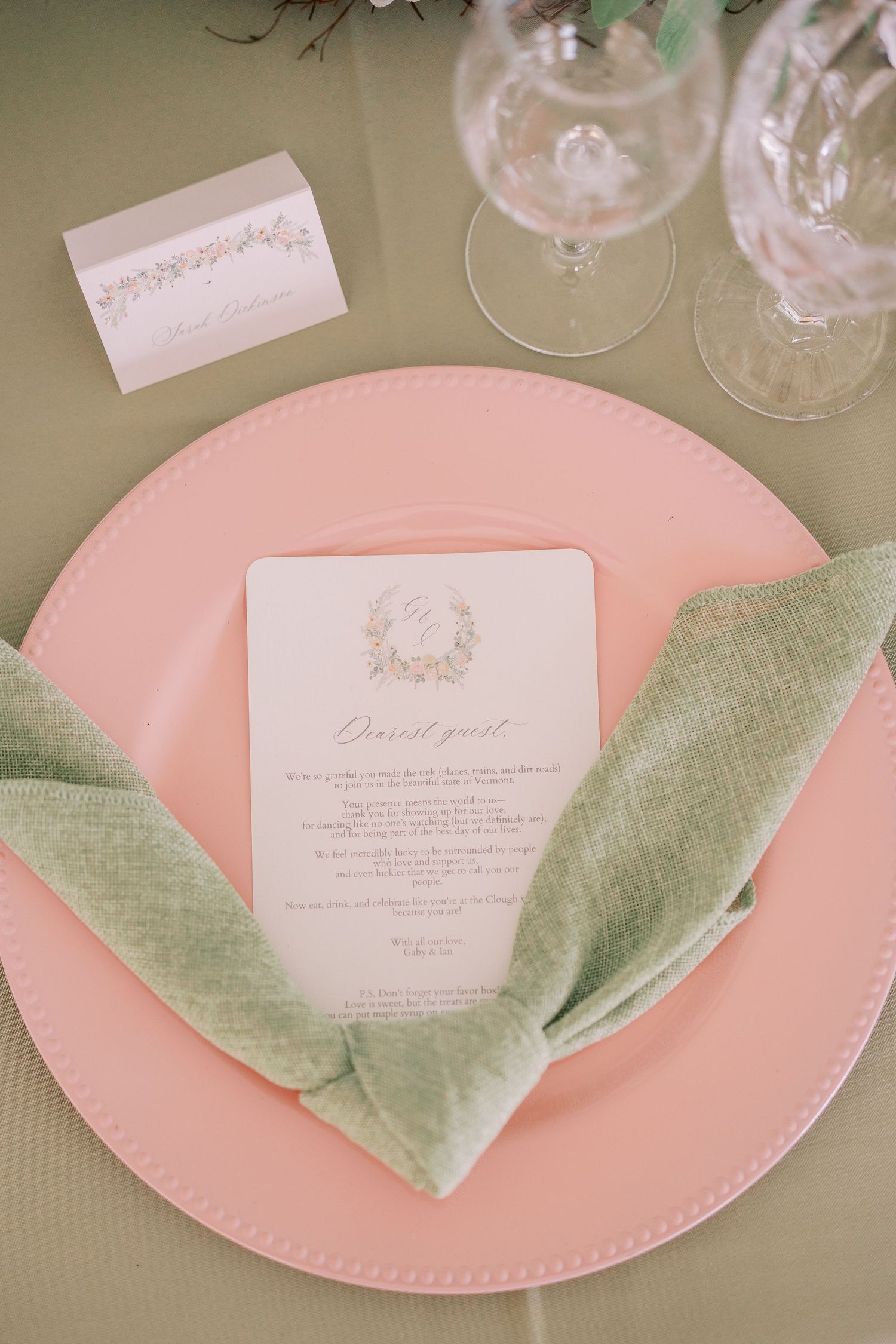 Table setting with pink plates and sage green linen napkins folded elegantly with white menu cards for a formal event.