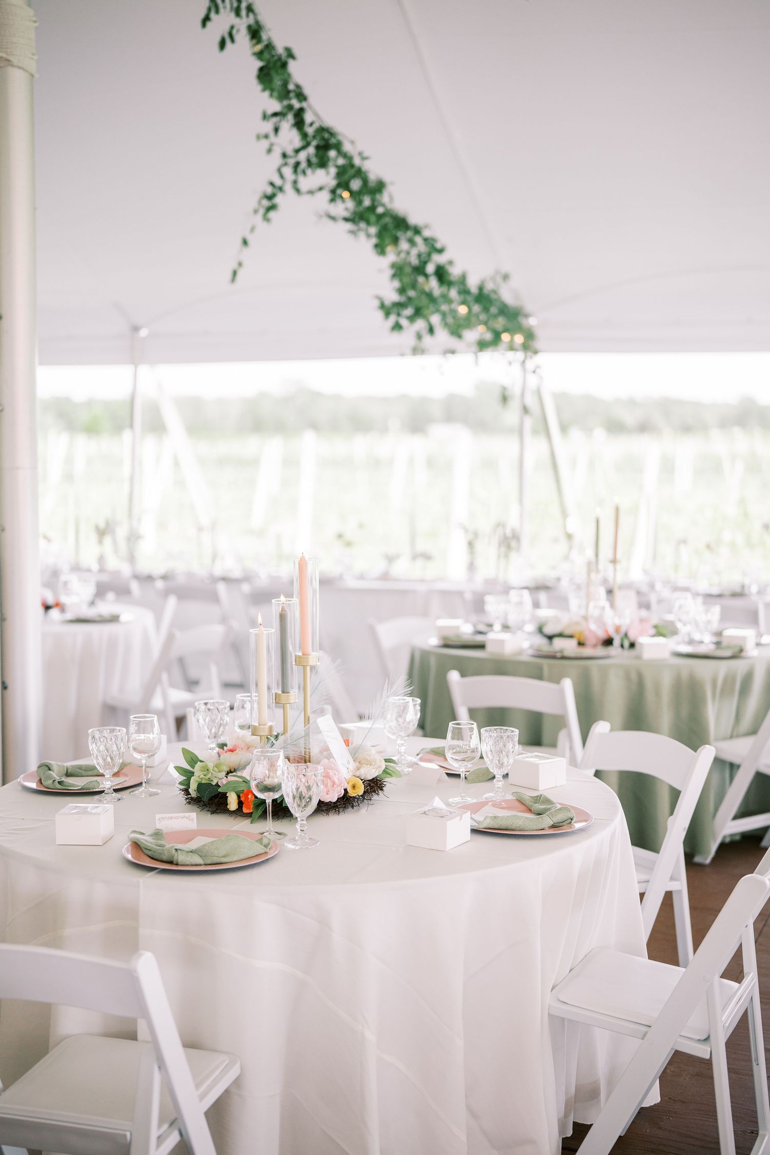 Elegant wedding reception table setup under a white tent with hanging greenery and taper candle centerpieces.