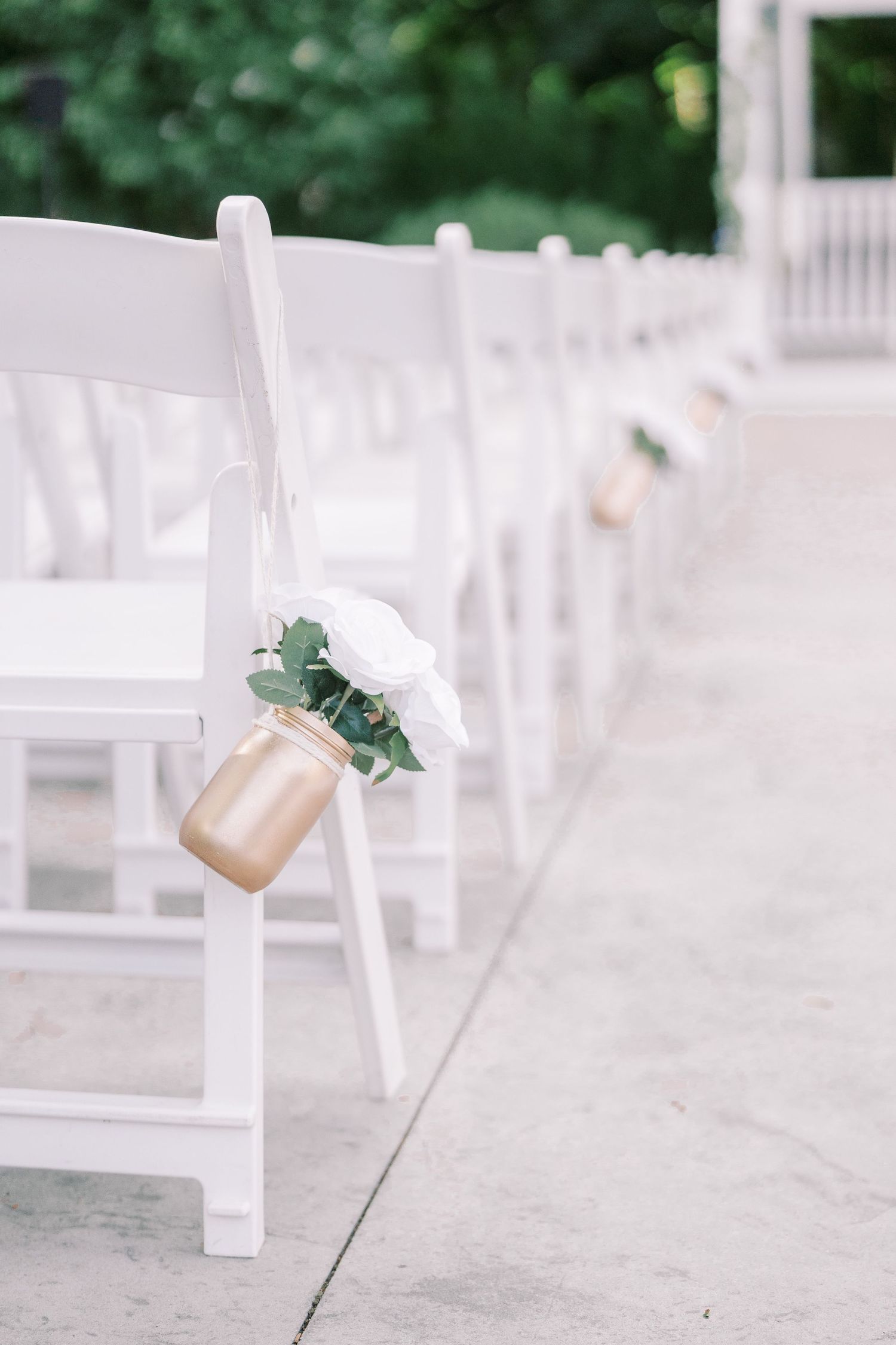 White folding chairs line a wedding ceremony aisle with mason jars and eucalyptus decorating the seats.