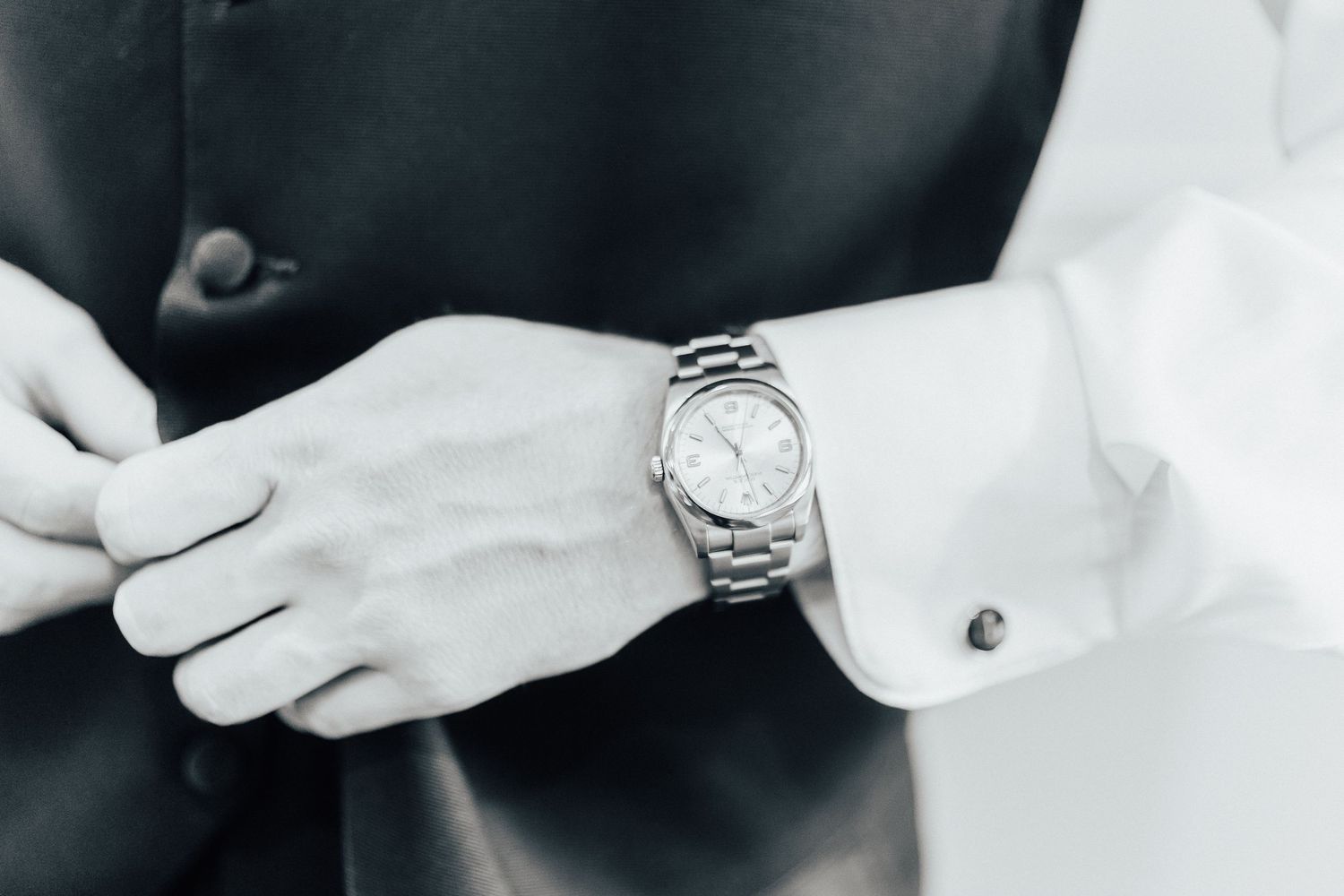 Black and white close-up of an elegant silver wristwatch worn with formal attire showing white cufflinks.