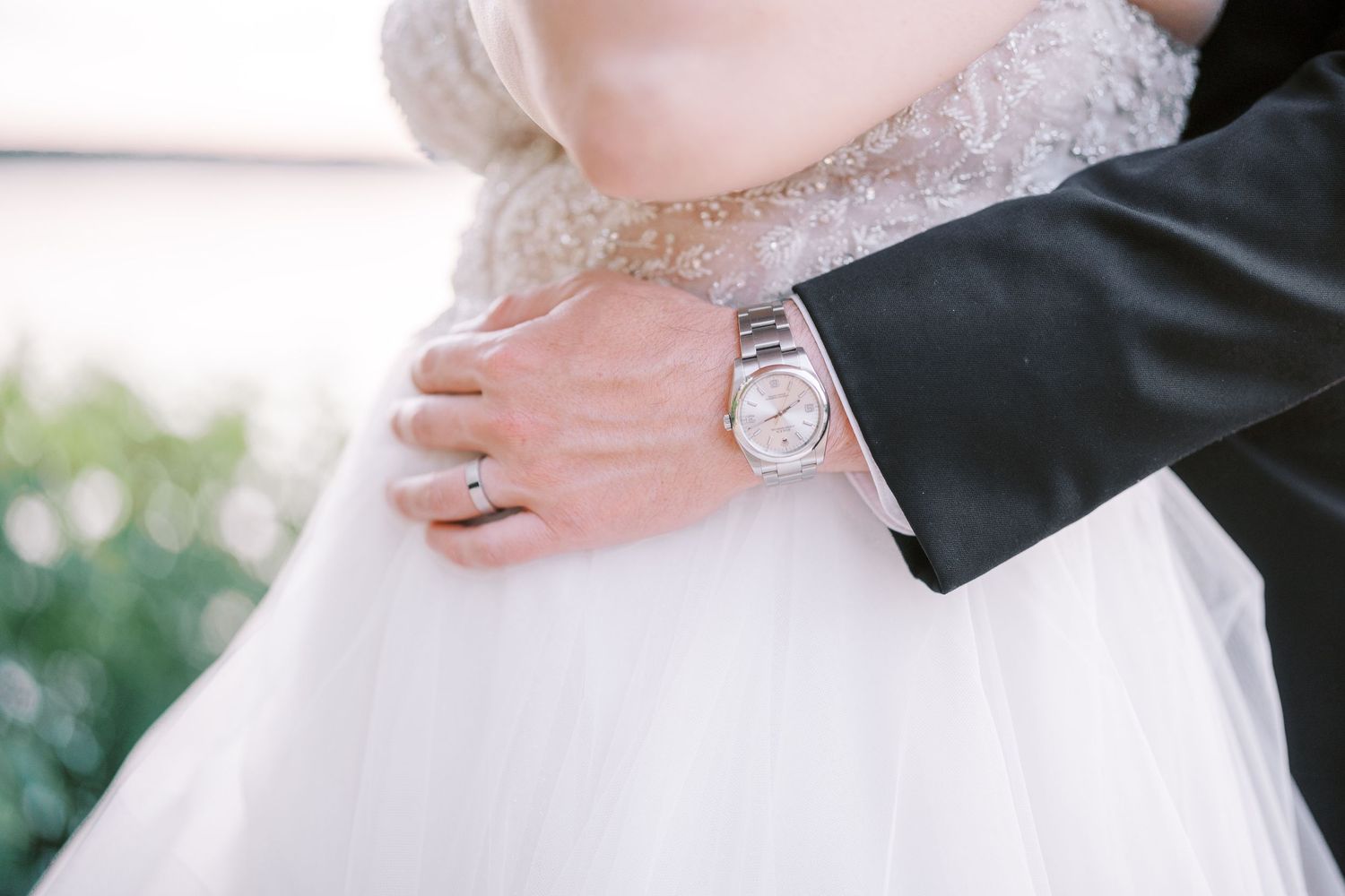 A close-up detail photo of a formal white wedding dress and delicate lace sleeve with diamond bracelet accessories.
