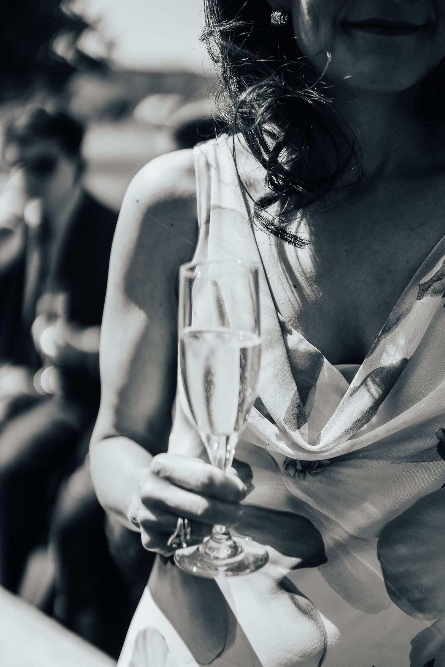 Person in a white dress holding a glass of champagne with windswept hair in black and white photography.