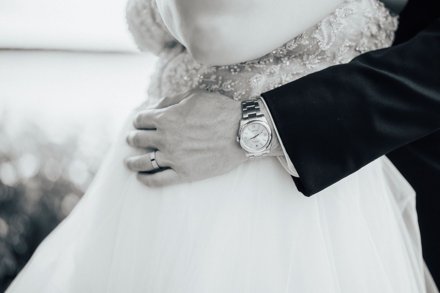 Close-up detail of hands wearing wedding rings and an elegant wristwatch against formal wedding attire.
