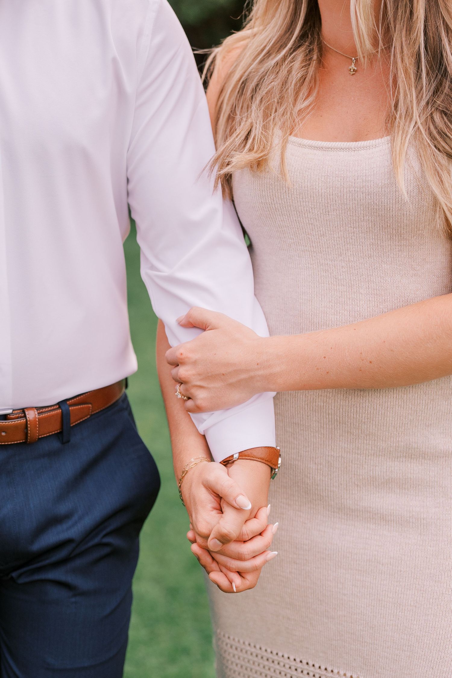 Close up view of couple holding hands with cream dress and white shirt against greenery background.