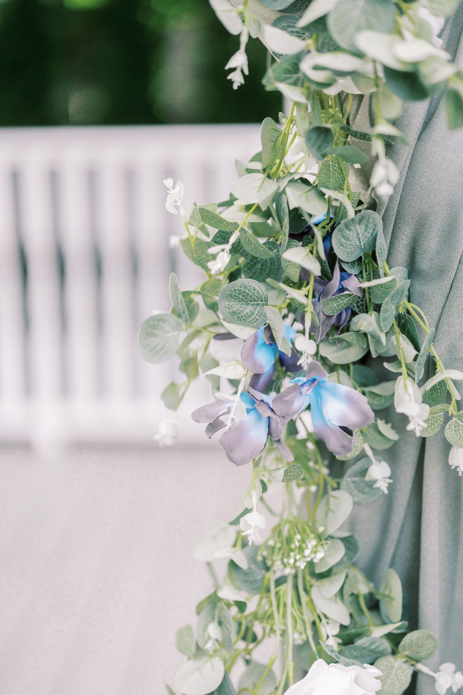 Delicate white floral arrangement with blue accents and eucalyptus leaves on a soft gray fabric background.