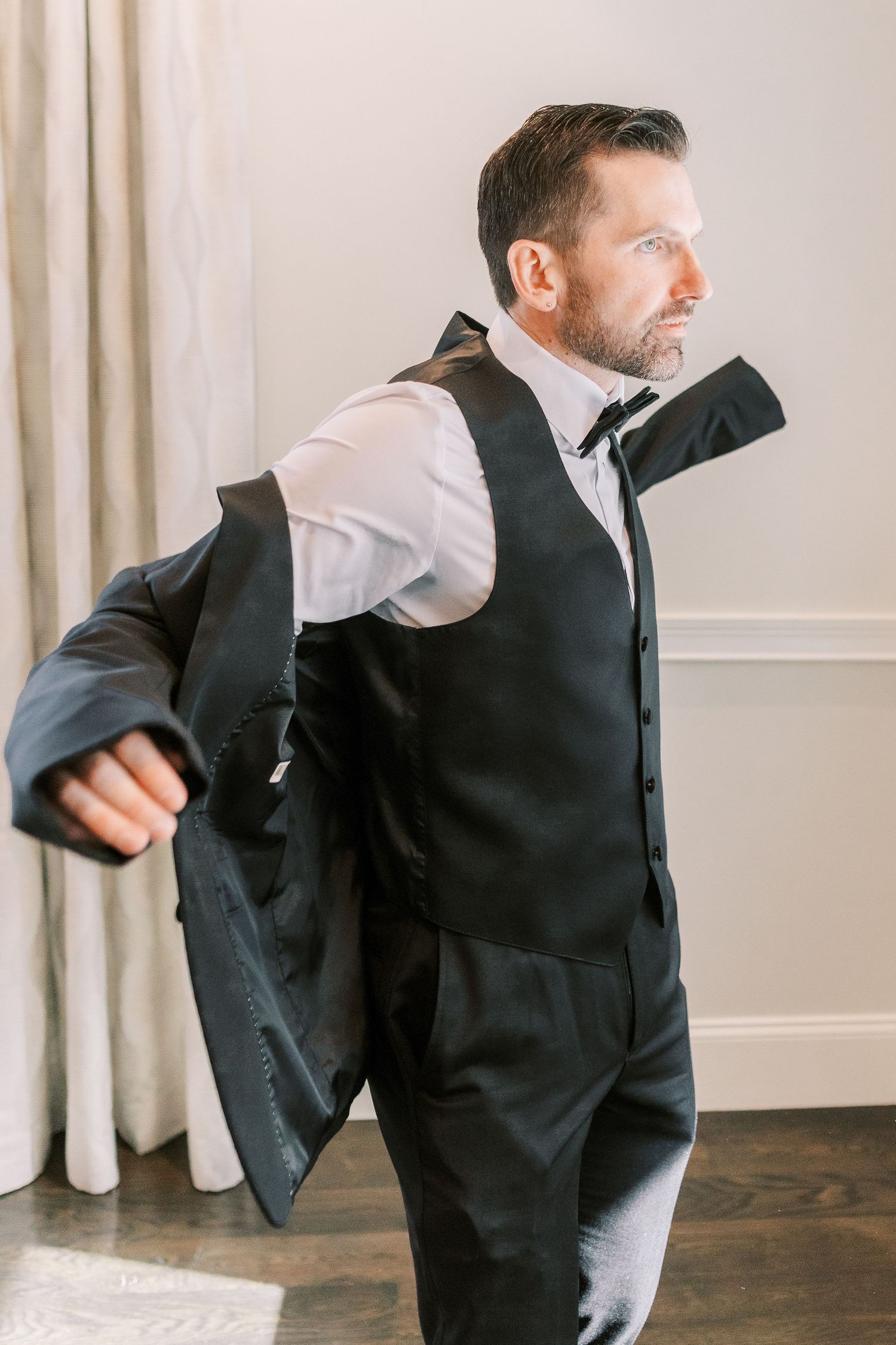 Professional in black suit and white shirt demonstrates dynamic dance moves in sequence against neutral wall background.