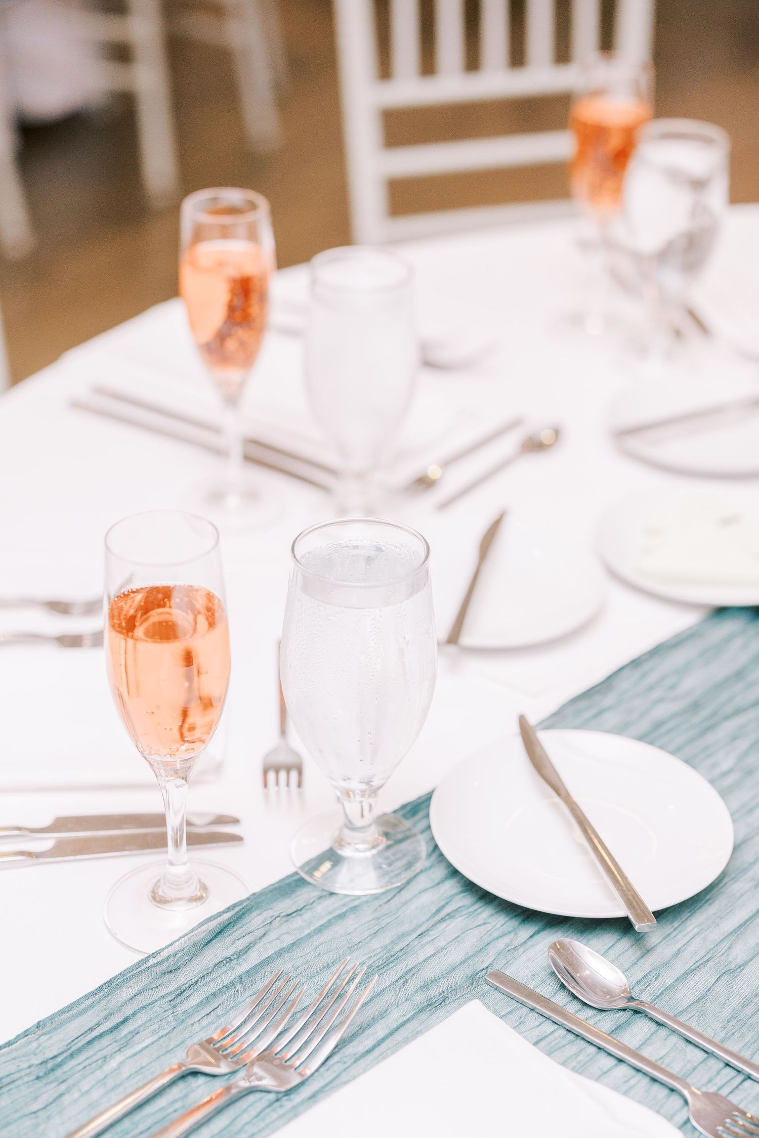Place settings with elegant white plates, metallic cutlery, and drinking glasses on a light blue tablecloth at a formal event.