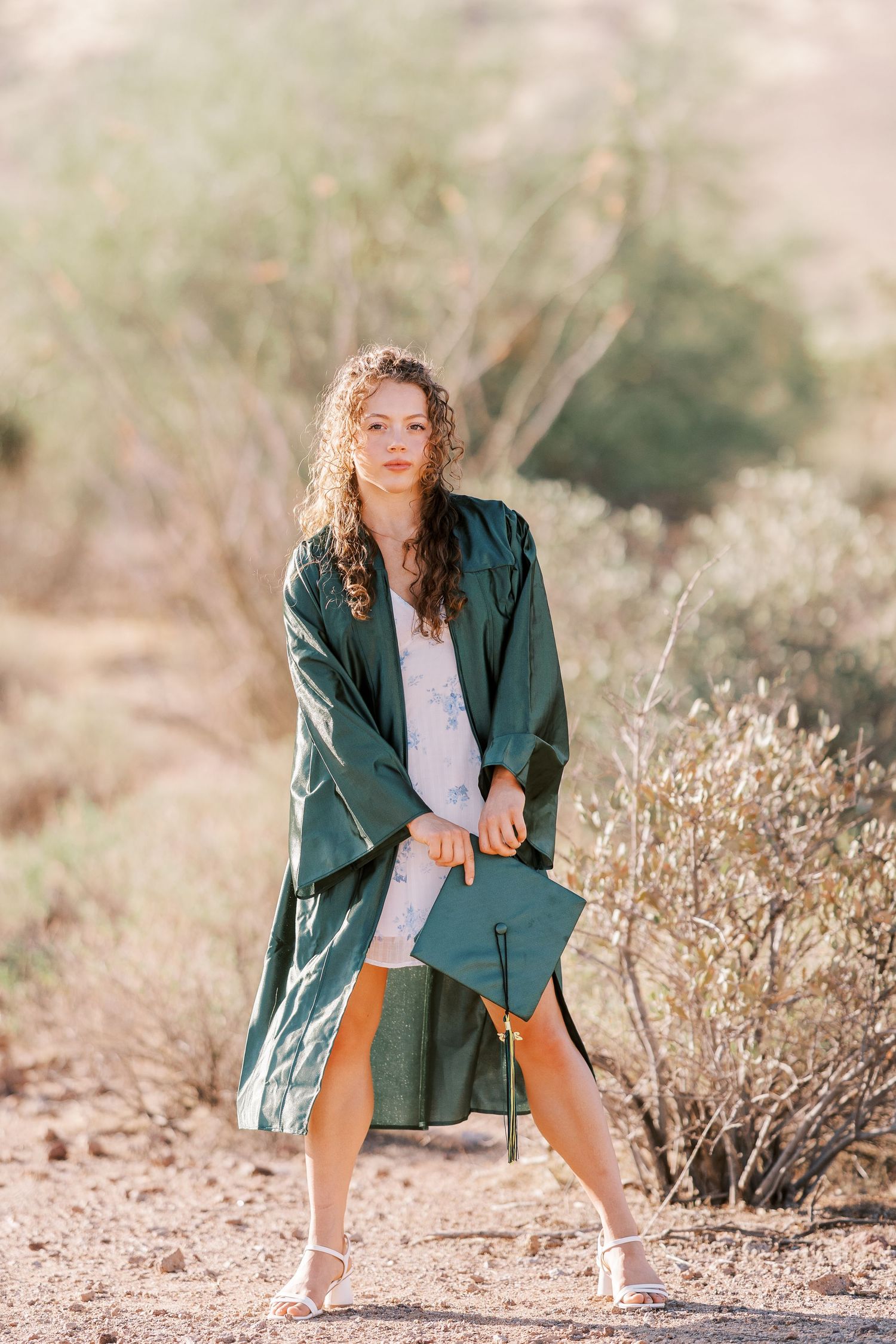 Outdoor graduation photo showing emerald green cap and gown against a desert landscape with sunlit natural backdrop.