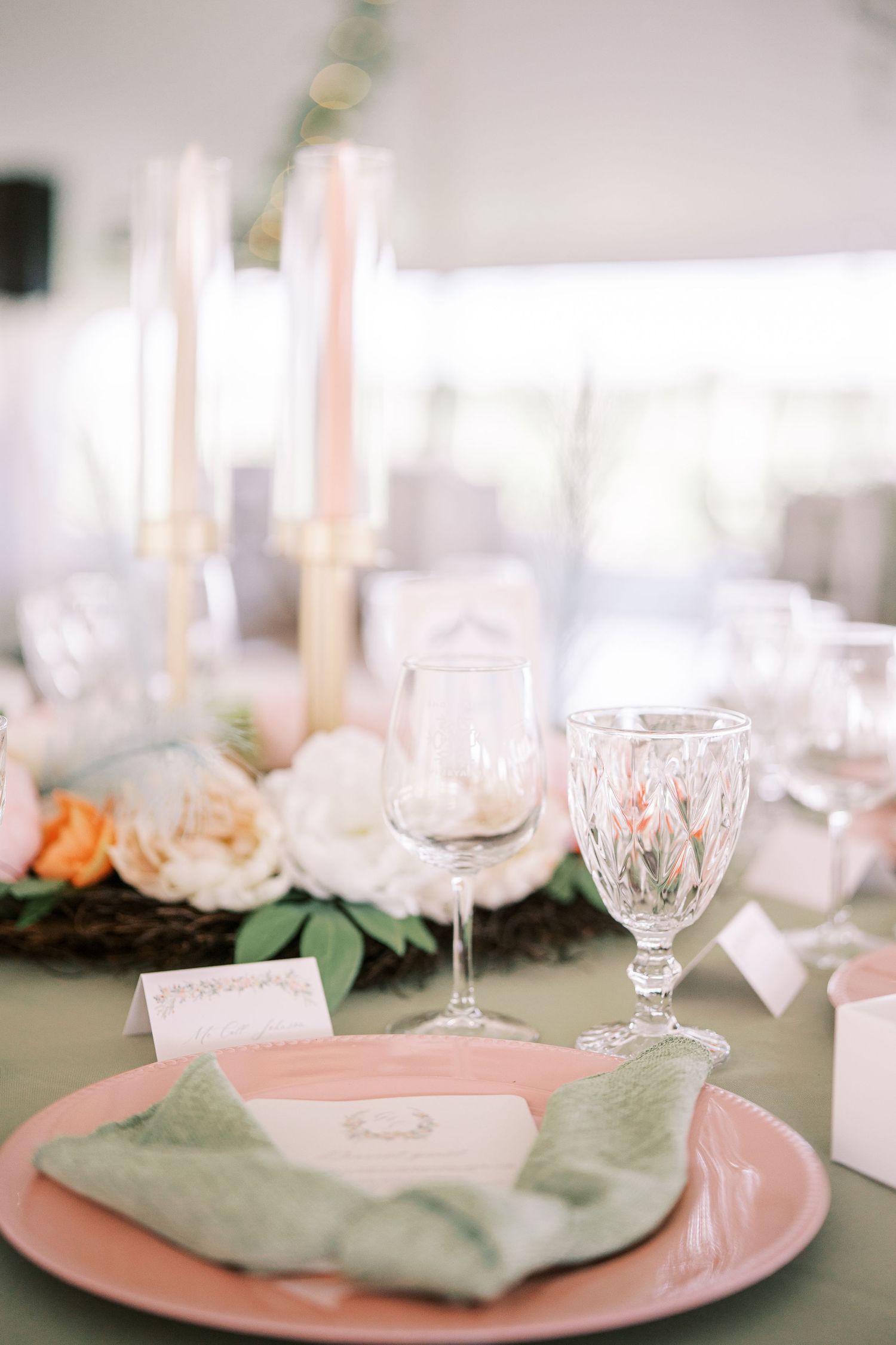 Elegant table setting with pink charger plates, sage green napkins, and crystal glasses for a wedding reception.