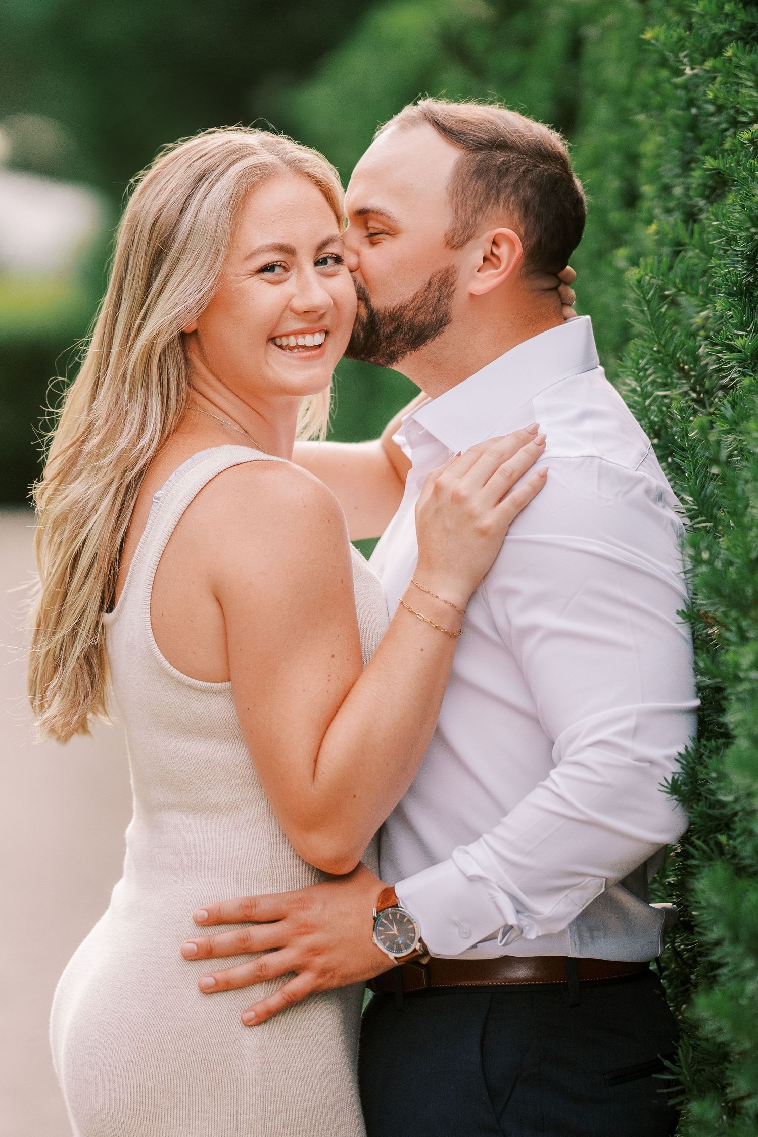 Romantic couple shares intimate playful moments together against a lush green backdrop in a series of photos.