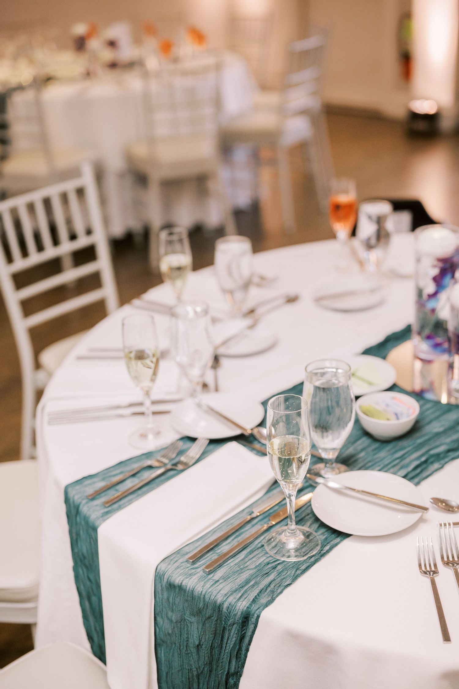 Elegant wedding reception table settings with crisp white linens and teal silk runners at a formal dining venue.