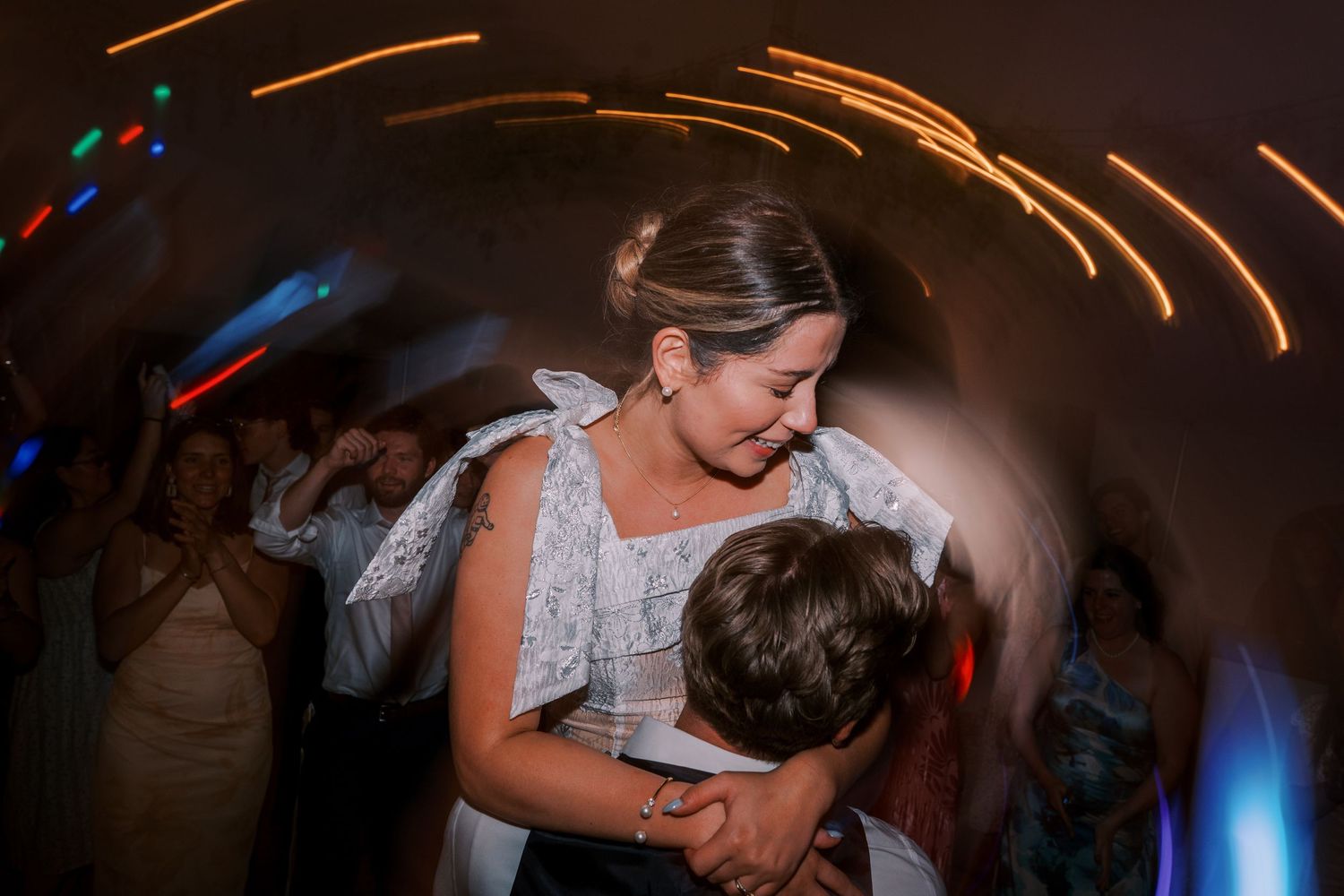 A couple shares a tender moment while dancing together at a wedding reception with motion-blurred lights in the background.