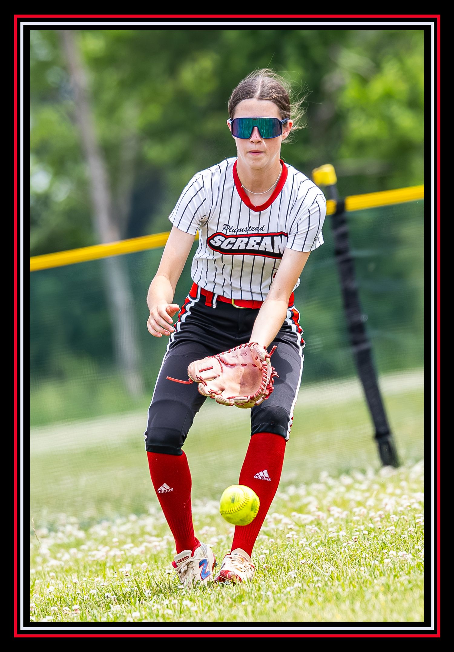 Female softball outfielder in Plumstead Scream uniform fielding a ground ball wearing sunglasses.