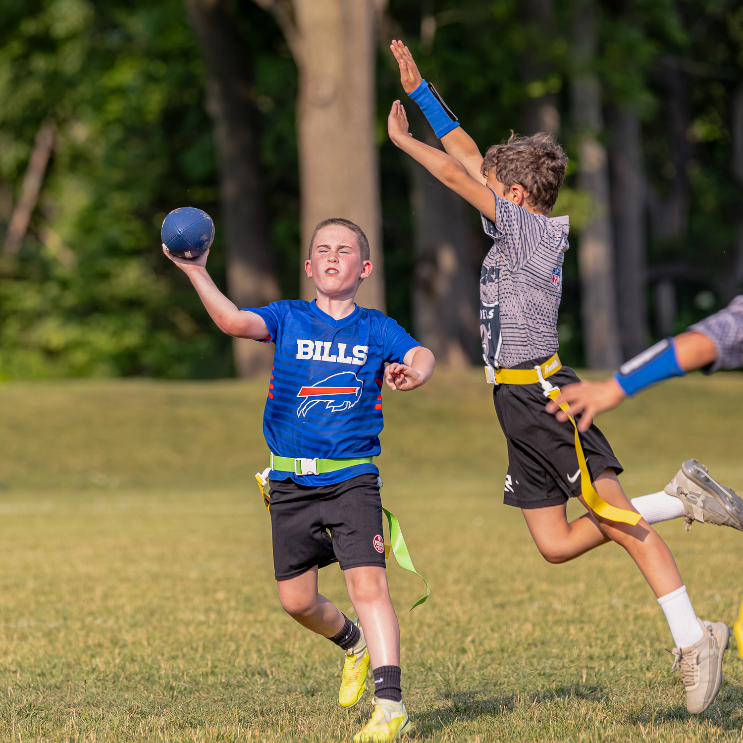 Boy in Bills jersey throws football while playing flag football outdoors on a sunny day.