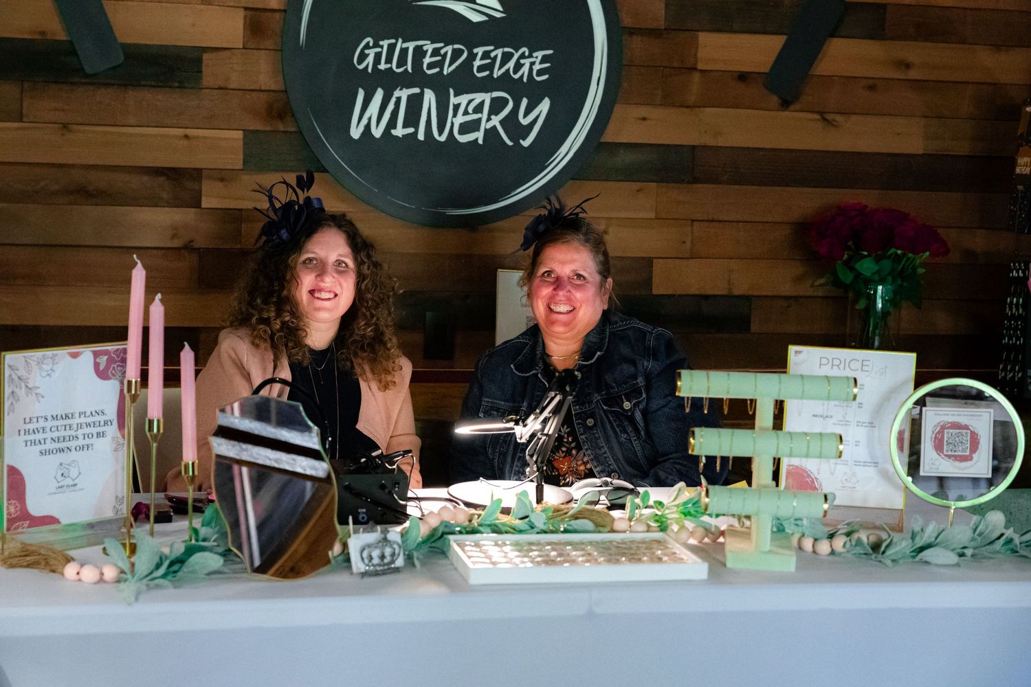 Two people staff a booth at Outer Edge Winery with wine bottles and displays on a decorated table.