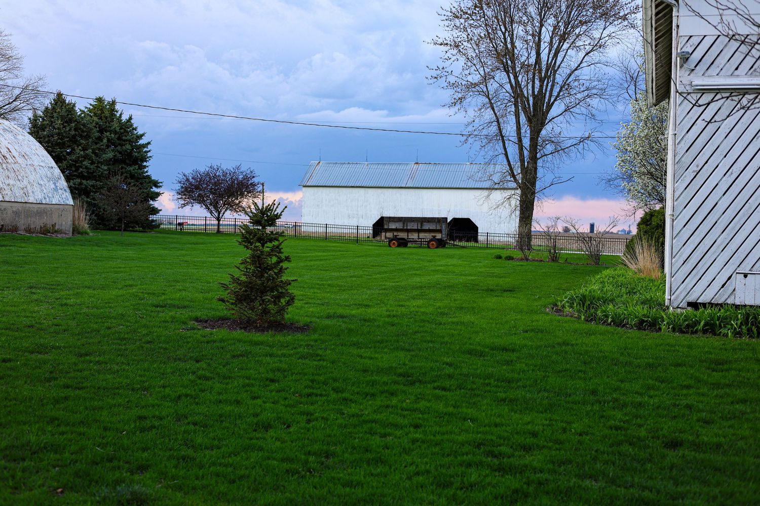Scenic farm view with white buildings, greenhouse and lush green grass under cloudy sky.