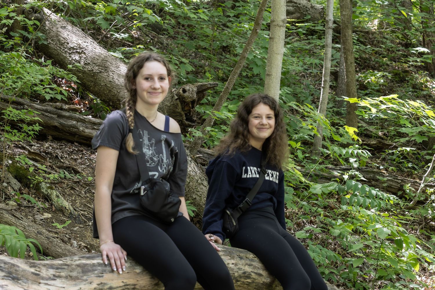 Two people in casual attire sitting on a rocky surface in a lush forest setting.