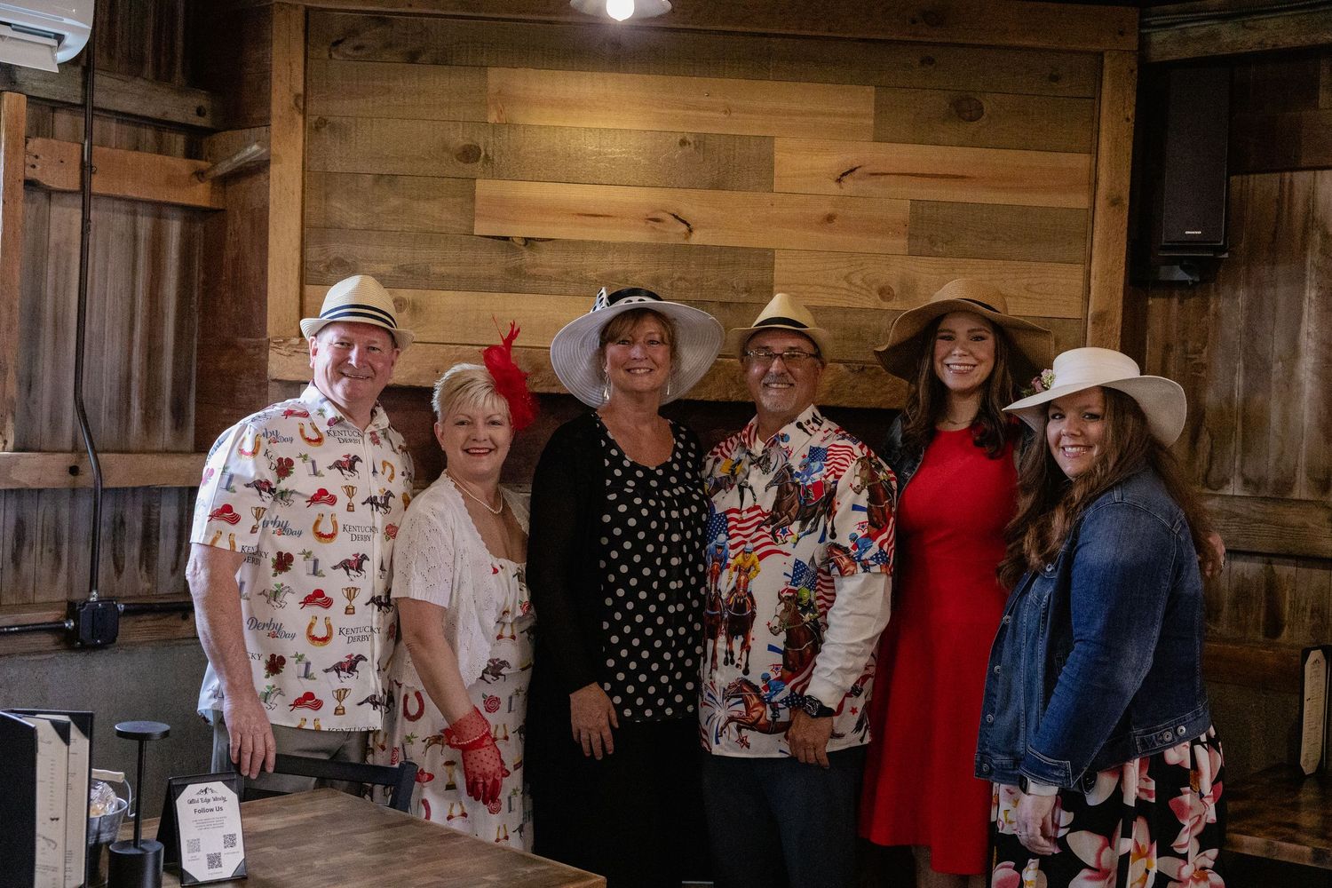 A group in festive attire poses together against a rustic wooden wall at what appears to be a casual gathering.