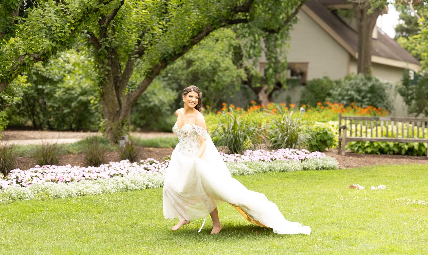 A flowing white wedding dress twirls gracefully on a lush green lawn with a garden backdrop.