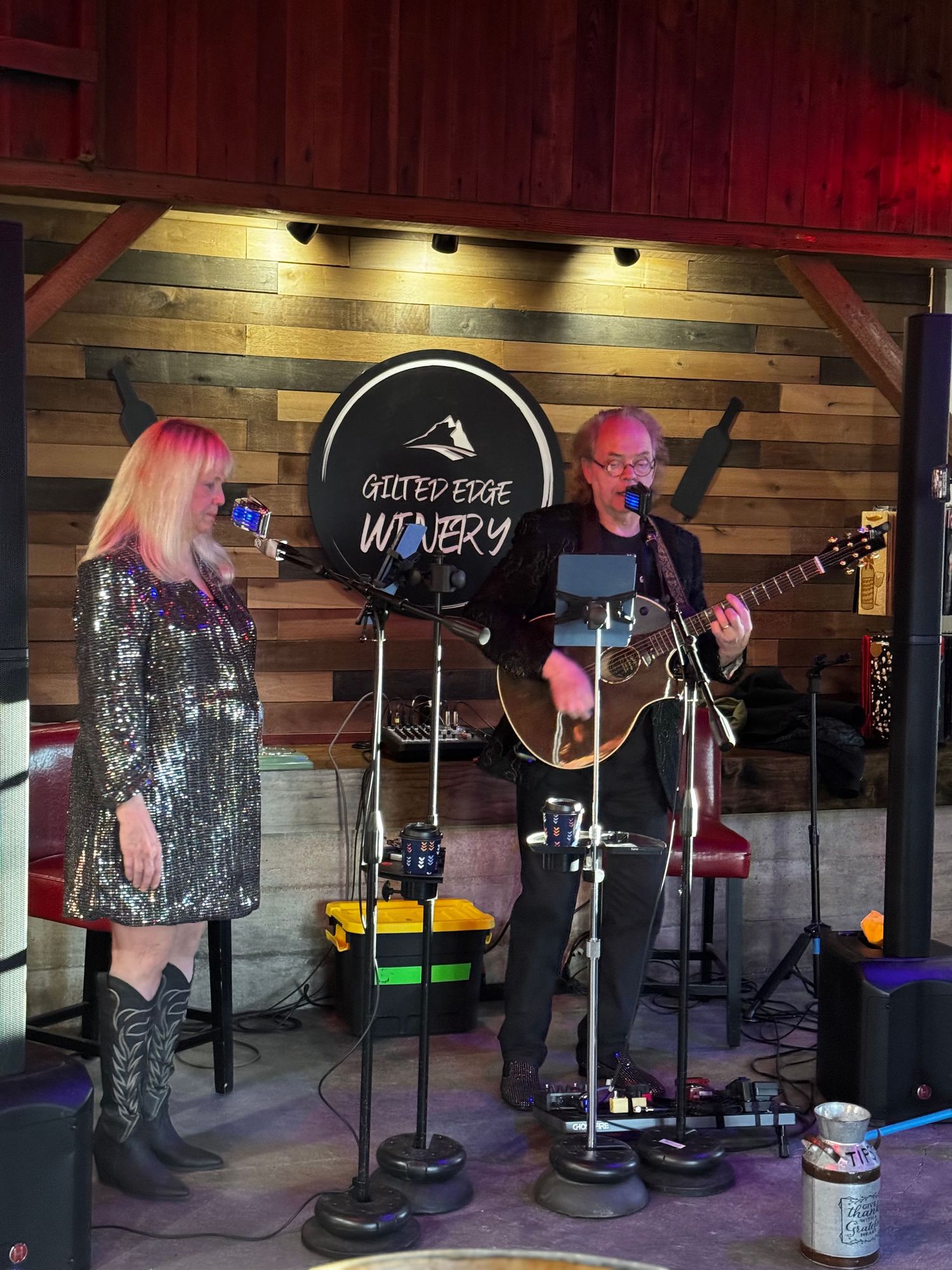 Musicians perform on stage at Outer Edge Winery with wooden wall backdrop and stage lighting.