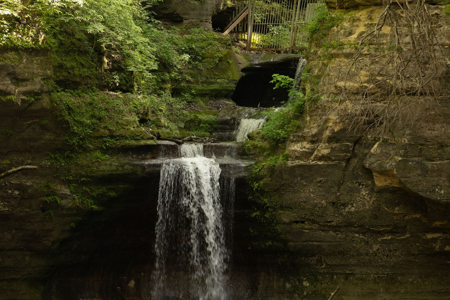 Scenic waterfall cascades down mossy rock cliffs in a lush forest setting creating a peaceful natural landscape.