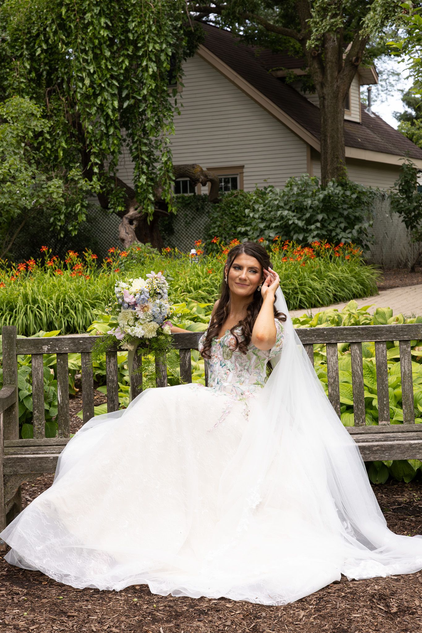 A wedding dress with a flowing white skirt and beaded bodice displayed in a garden setting with orange flowers and greenery.