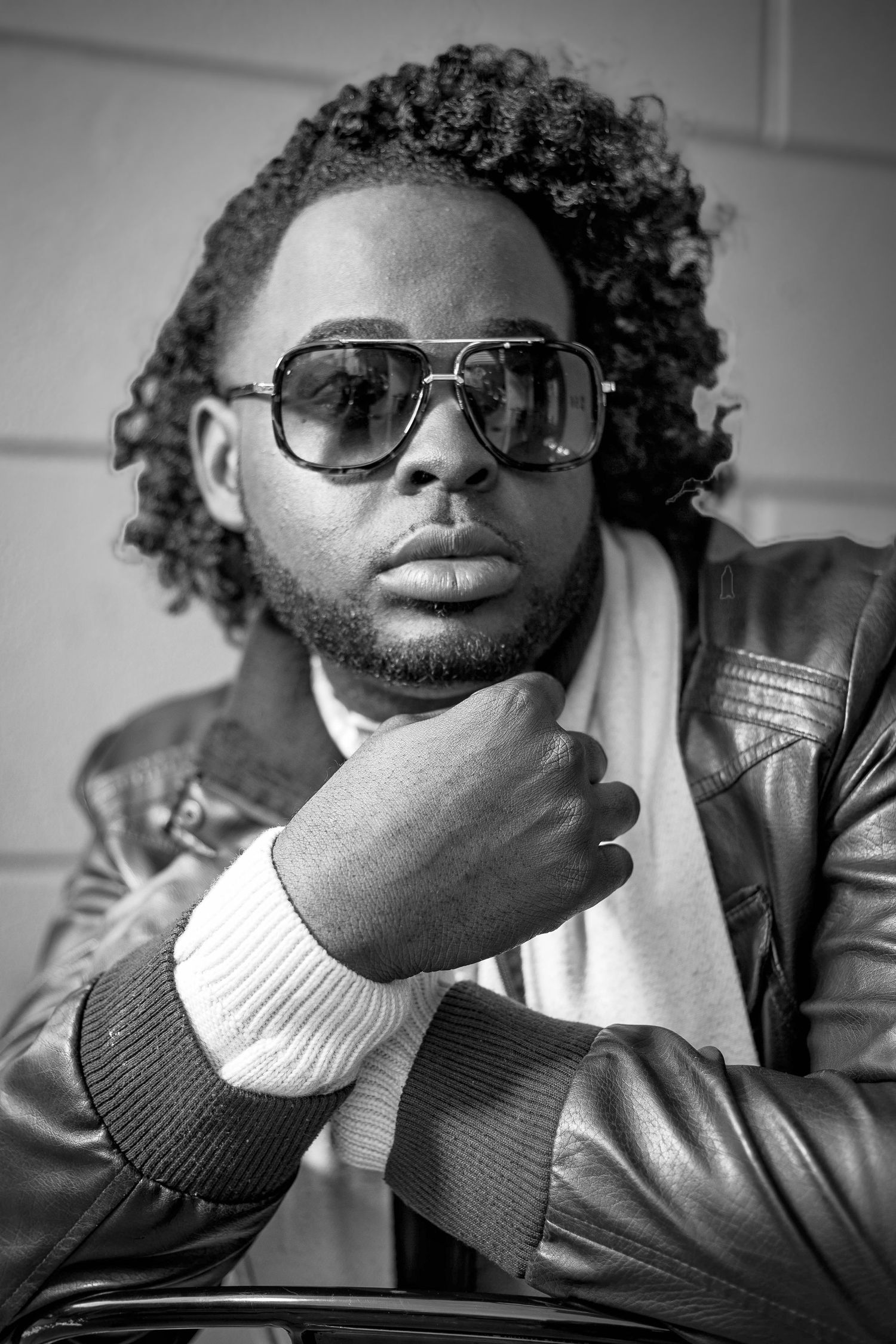 Black and white portrait with aviator sunglasses wearing leather jacket and scarf.
