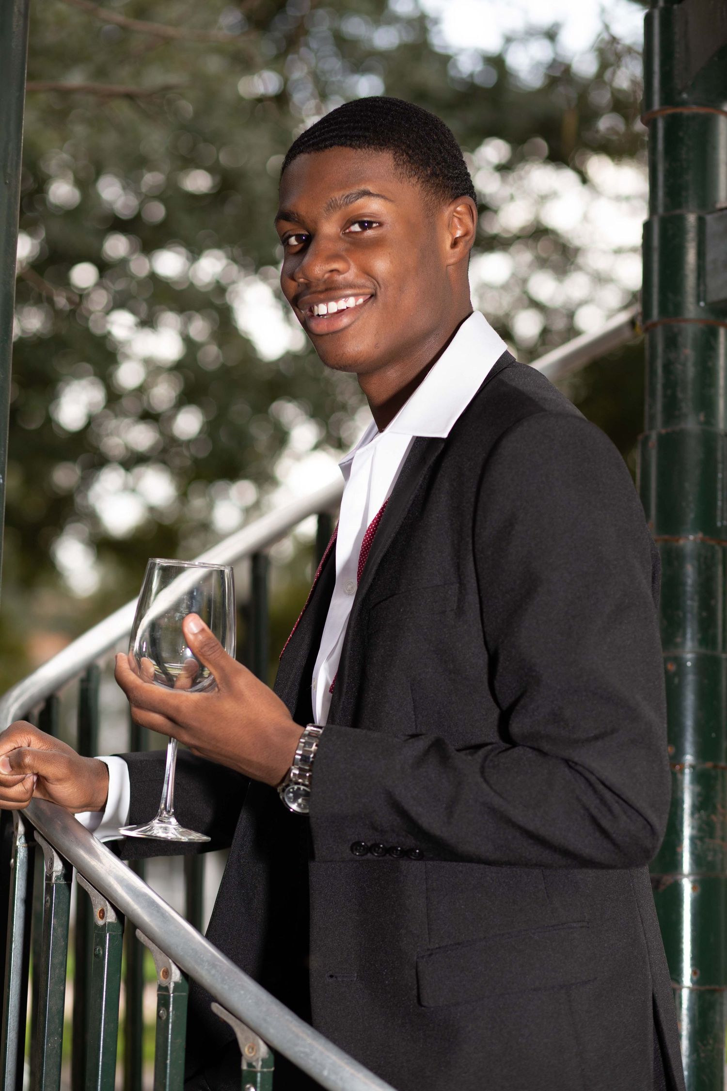 Person in formal suit holding champagne glass on outdoor balcony.