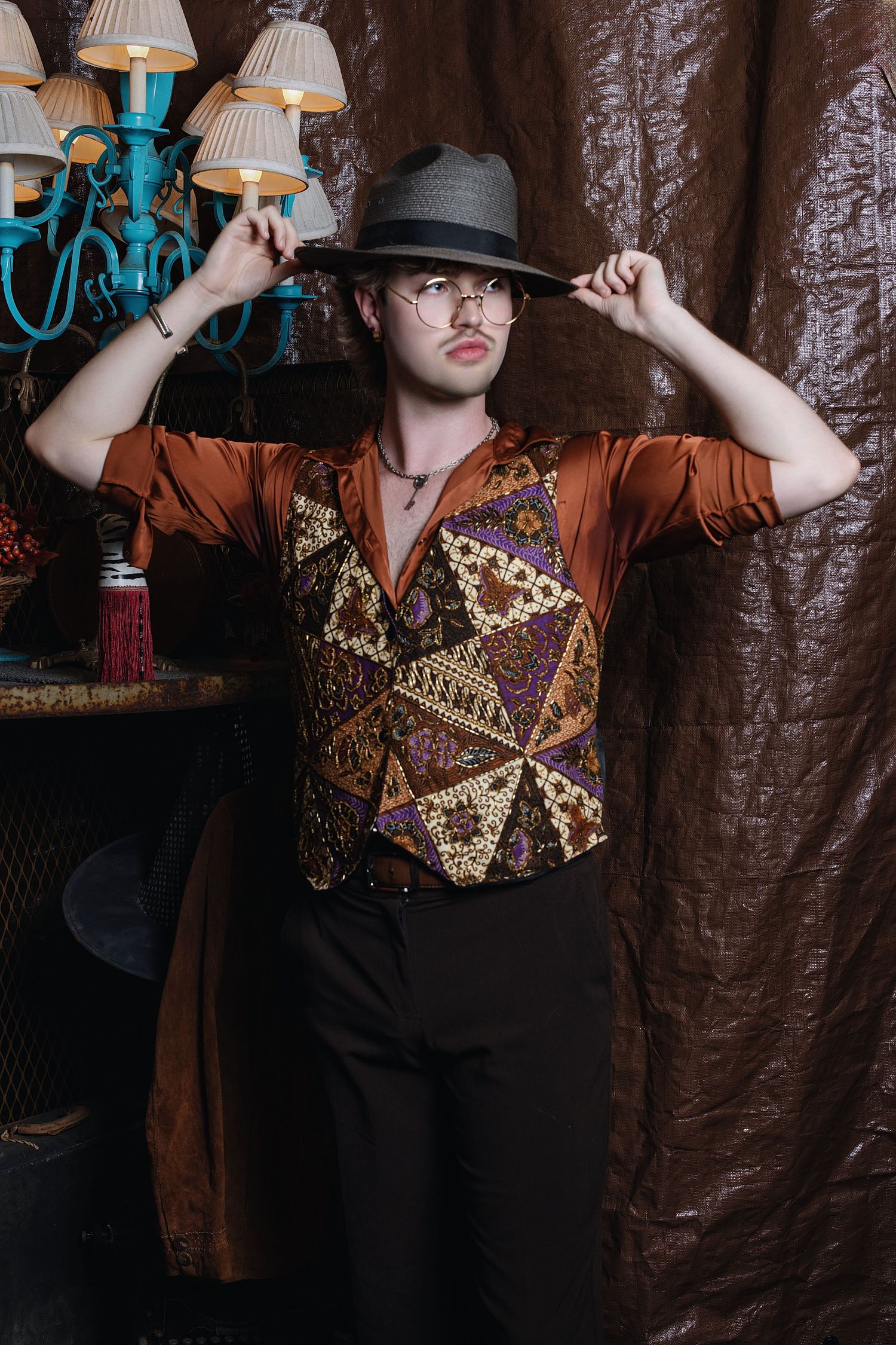 A figure in a patterned shirt and hat poses dramatically against a dark curtain backdrop in a series of artistic shots.