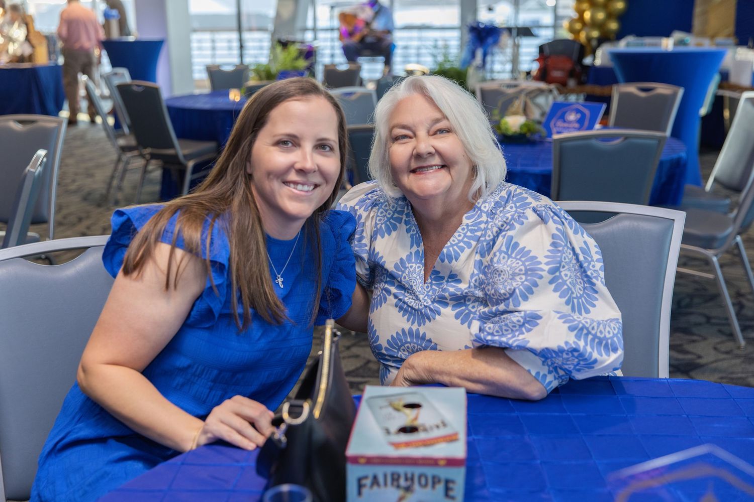 People in blue and white attire gather at tables in a bright modern office or conference space.