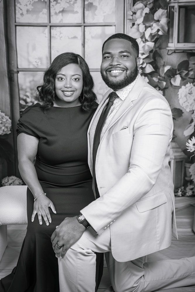A couple poses together for engagement photos, with one wearing a black dress and the other in a white suit.