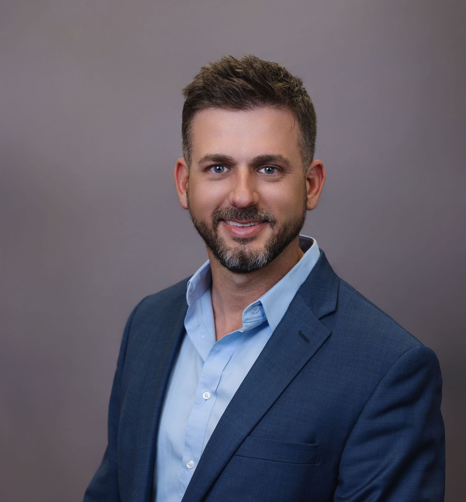Professional headshot of businessman in navy suit and light blue shirt.
