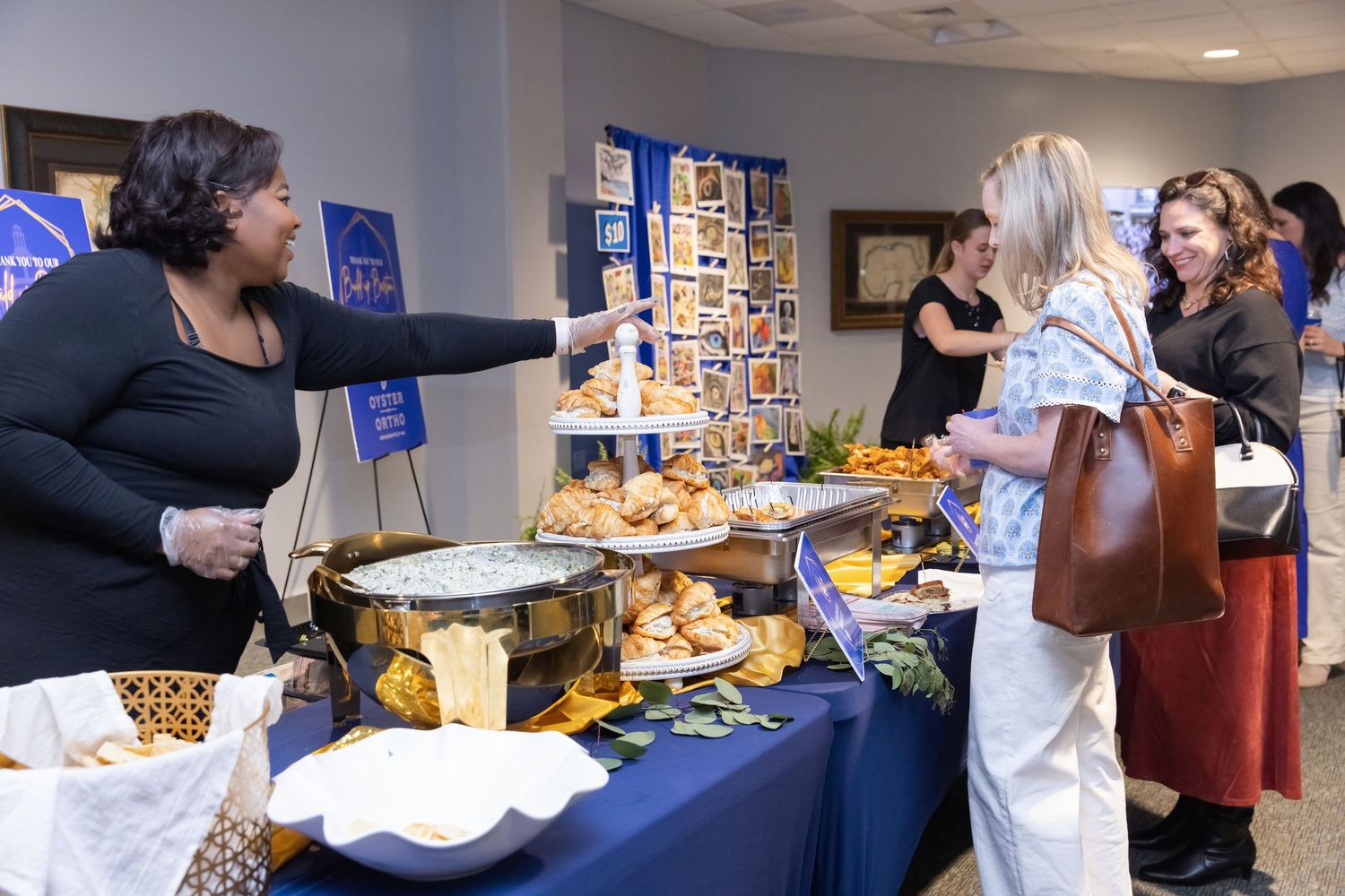 People browse and select items at a busy buffet table during a catered event.
